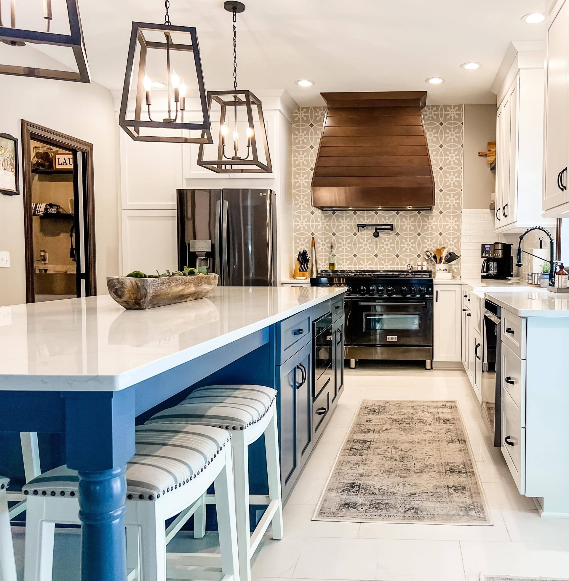White shaker kitchen with navy island, wood range hood, patterned cement tile backsplash, white quartz counters, lantern pendants