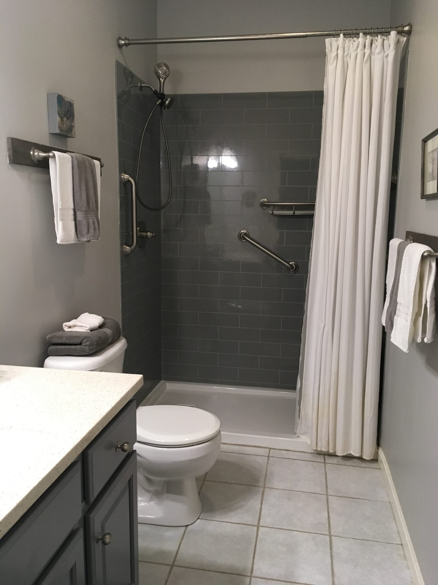 Bathroom with grey subway tile tub surround, curved shower-curtain rod, grab bar, and dark counters