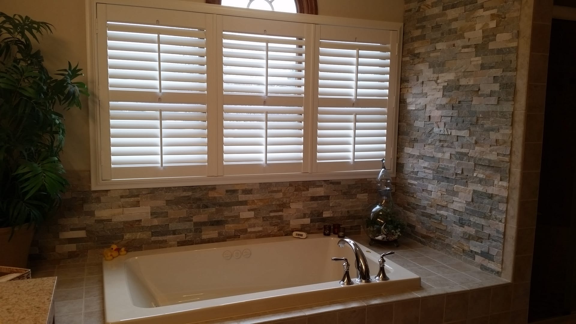Bathroom with drop-in soaking tub, stacked-stone accent wall, white plantation shutters, and tile deck, Edinboro