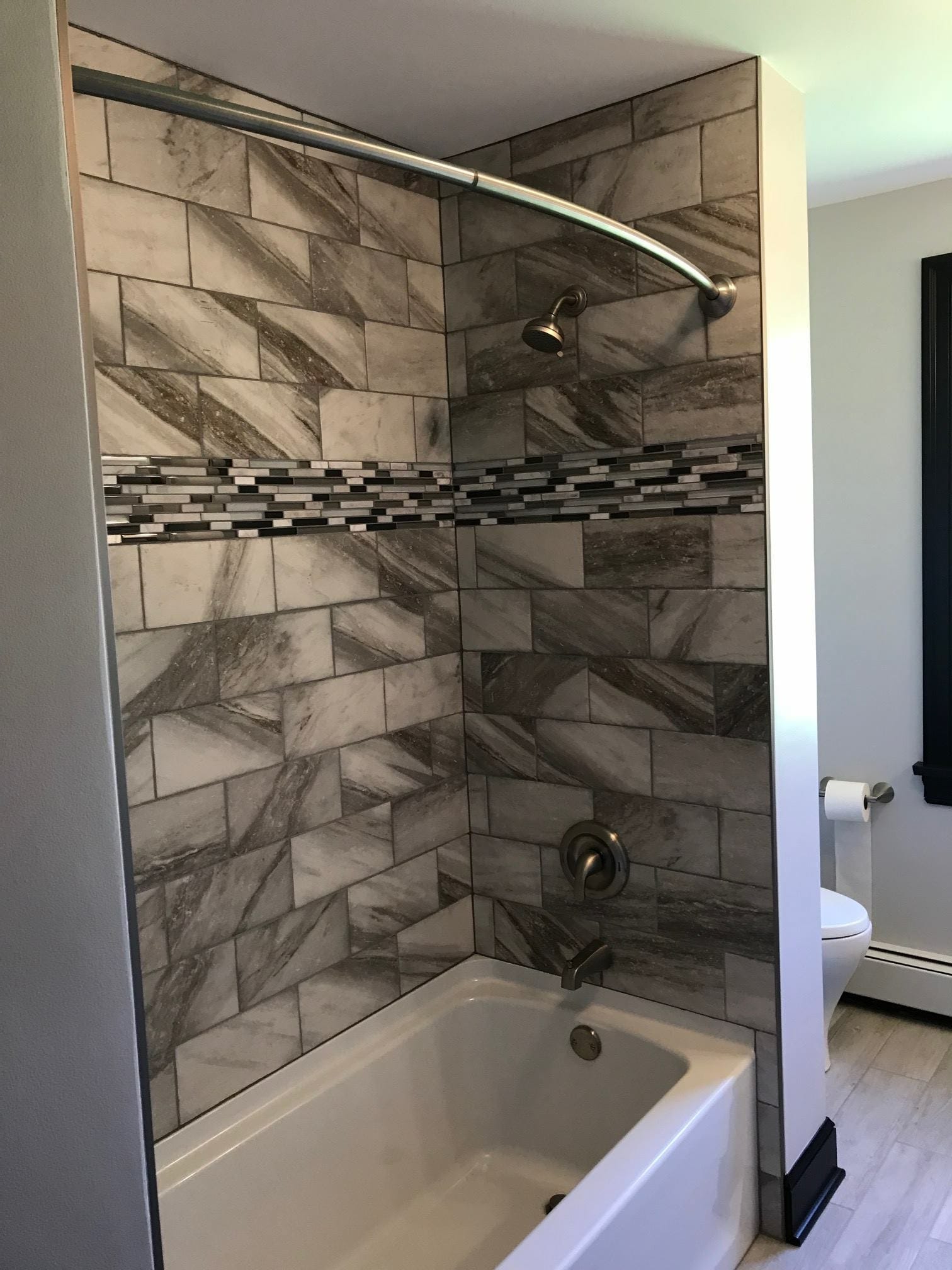 Tub-shower with grey marble-look tile surround, linear glass mosaic accent band, curved rod, and brushed-nickel fixtures, Erie PA