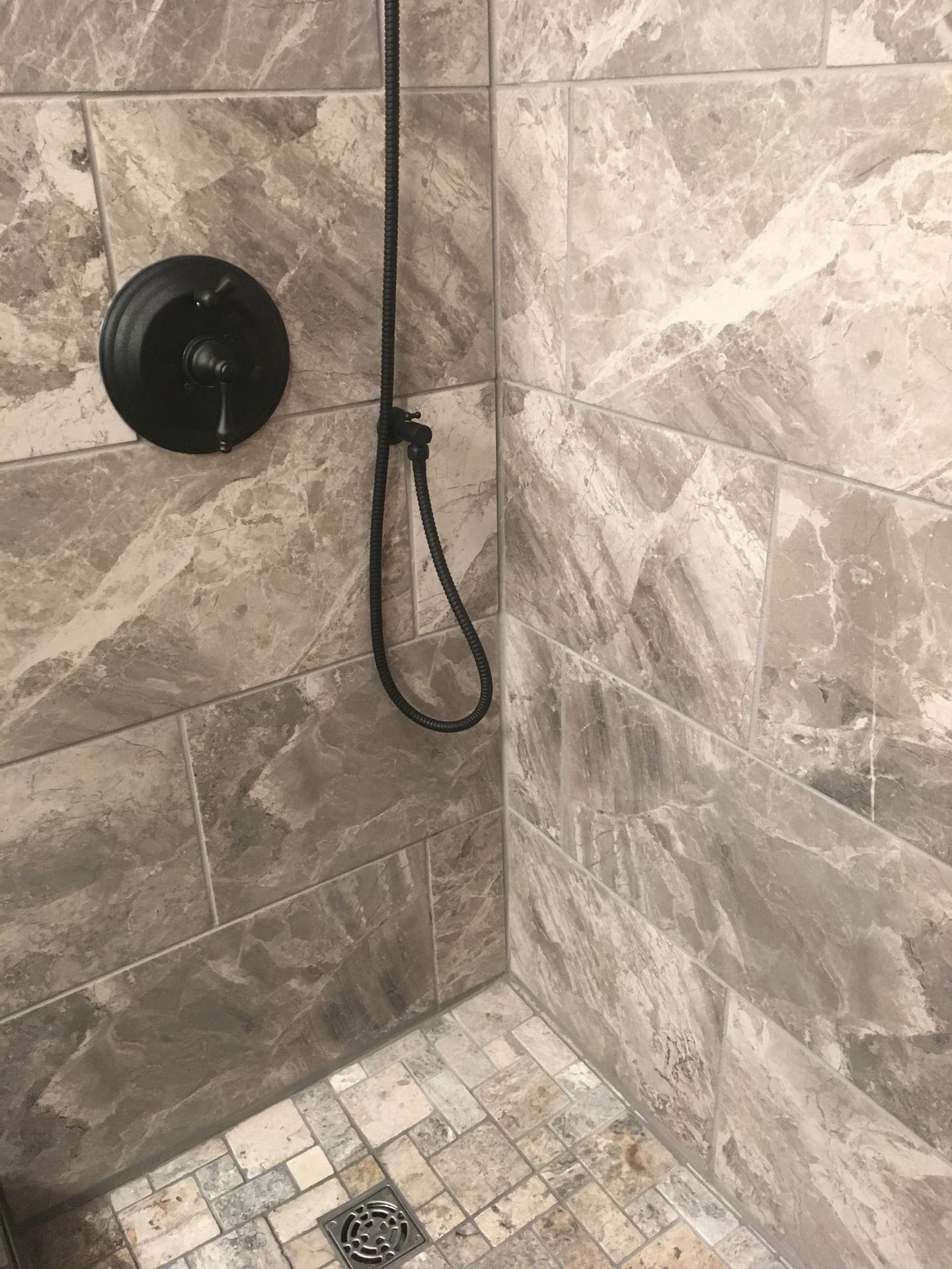 Tile shower with grey marble-look walls, matte-black rain and handheld shower, and stone mosaic shower floor, Edinboro