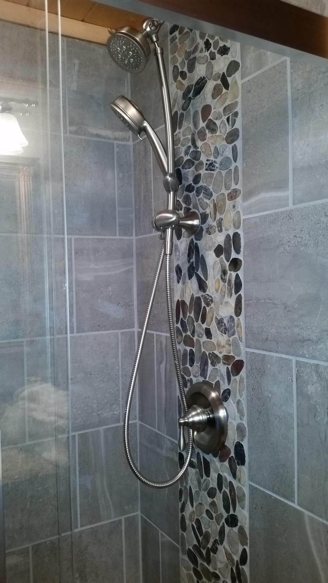 Tile shower with grey slate-look walls, multicolor pebble mosaic accent band, and brushed-nickel handheld shower