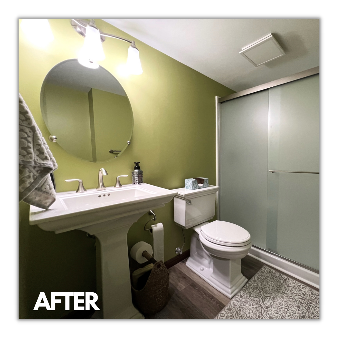 Green-walled bathroom with white pedestal sink, round mirror, sliding glass shower, and wood-look plank flooring, Erie County