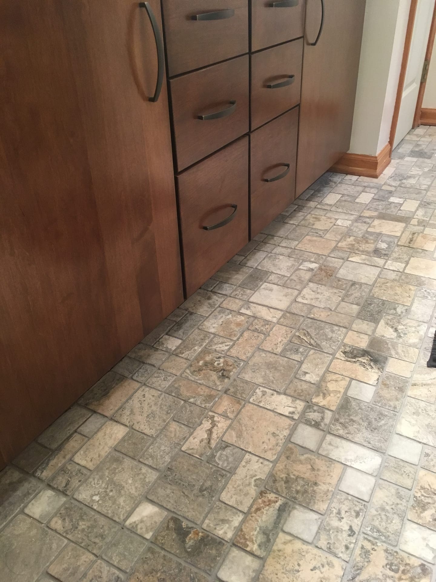 Natural stone brick-pattern tile wall beside a wood vanity with chrome pulls