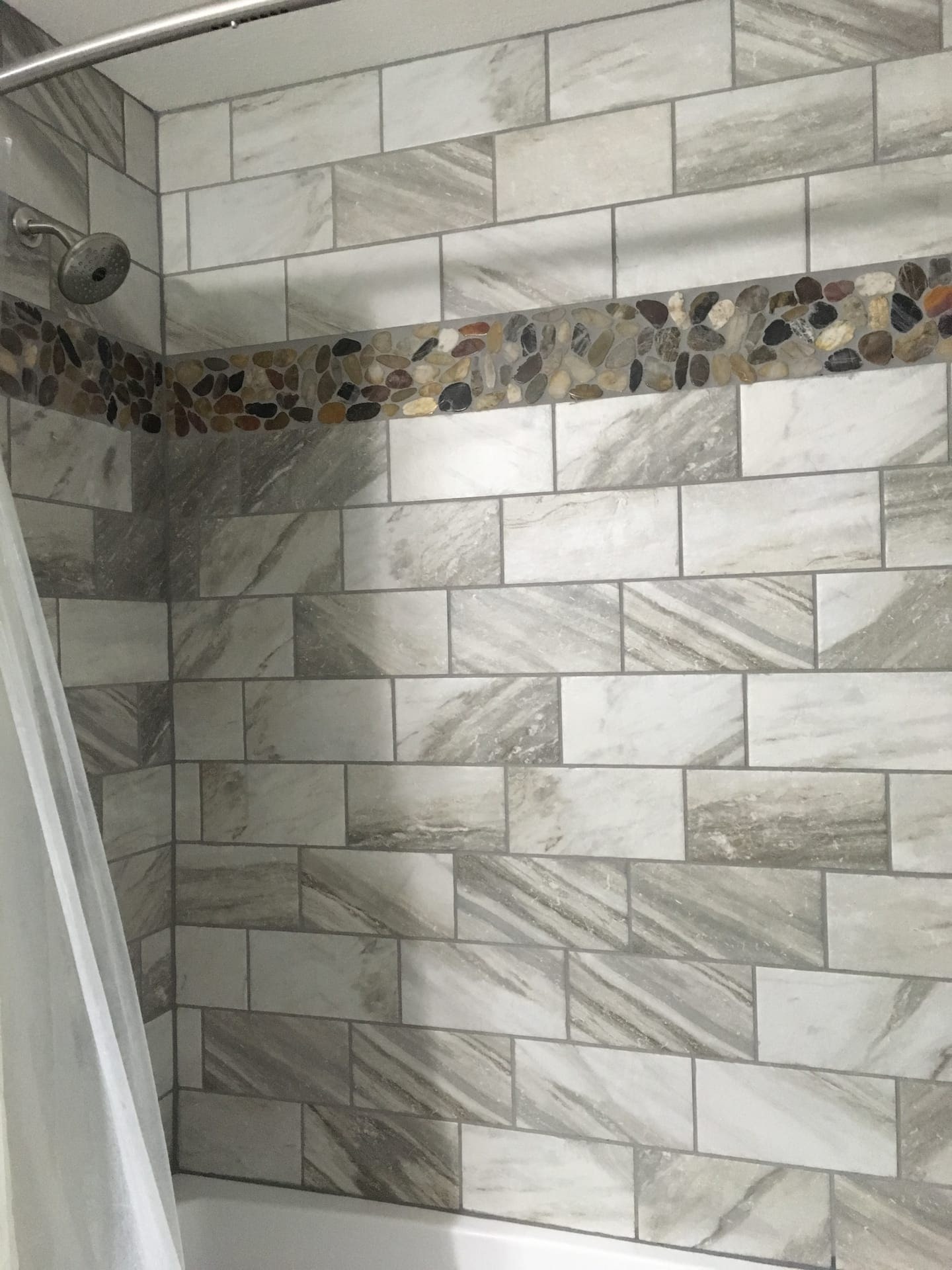 Tile shower with grey marble-look stacked tile, vertical pebble mosaic accent strip, and glass enclosure, Erie County