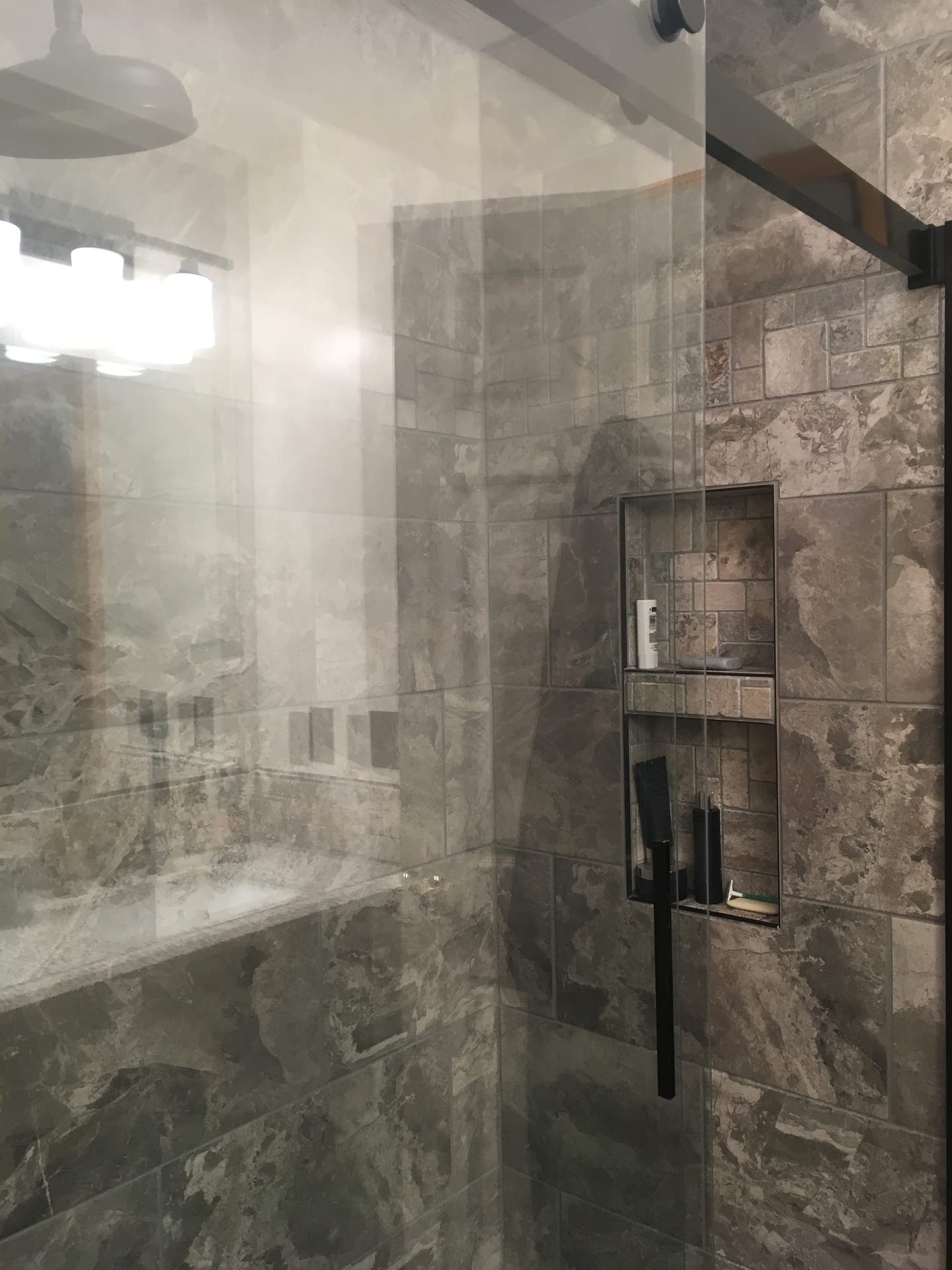 Tile shower with dark grey marble-look walls, recessed double niche, stone mosaic accent, and matte-black fixtures