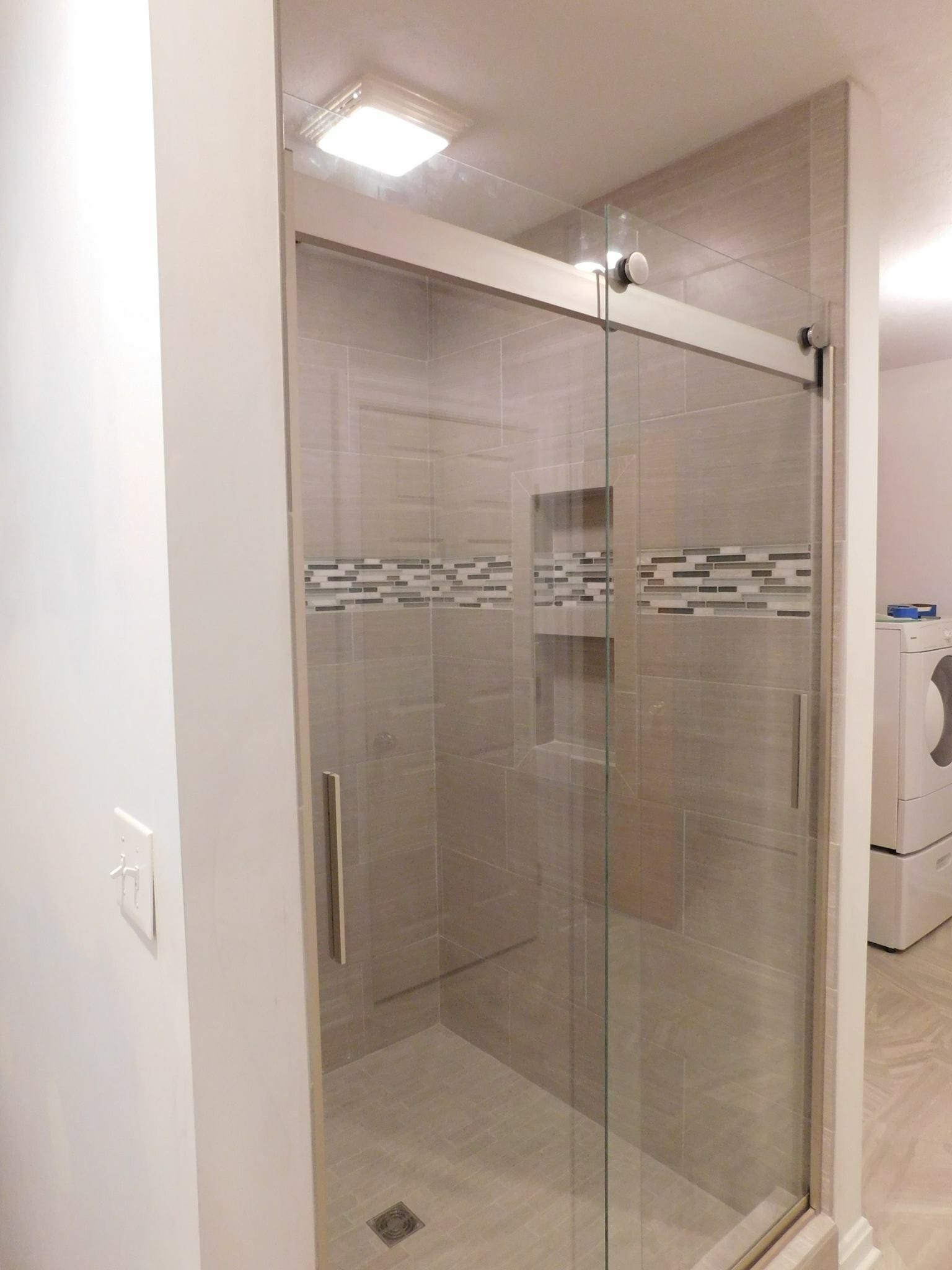 Bathroom with glass sliding-door tile shower, greige tile walls, linear glass mosaic accent band, and recessed niche
