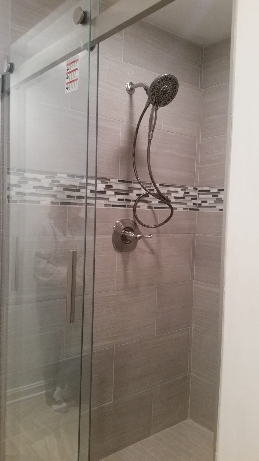 Tile shower with grey linen-look tile, vertical glass mosaic accent strip, brushed-nickel rain and handheld shower