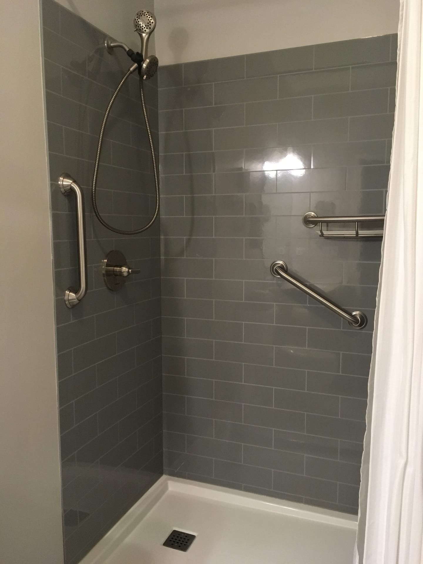 Tub-shower with grey subway tile surround, brushed-nickel rain and handheld shower, grab bar, dark tub deck, Erie County