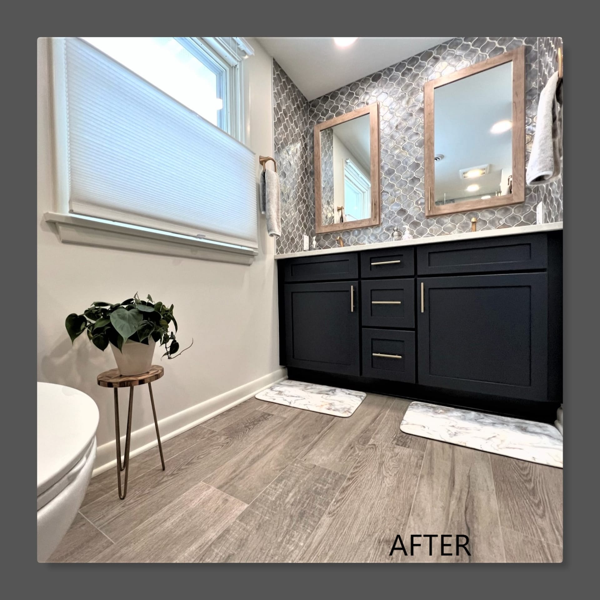 Bathroom double vanity with navy shaker cabinets, brass pulls, silver mosaic accent wall, wood-look plank flooring, Edinboro