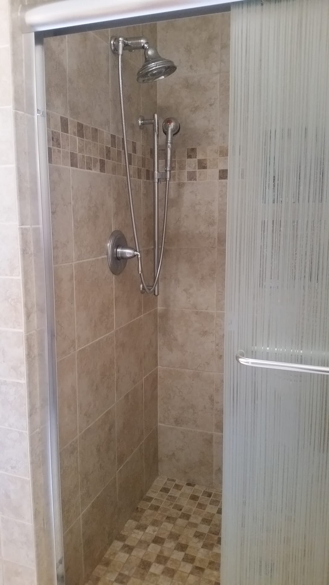 Tub-shower with travertine tile surround, natural stone mosaic accent bands, and brushed-nickel handheld shower
