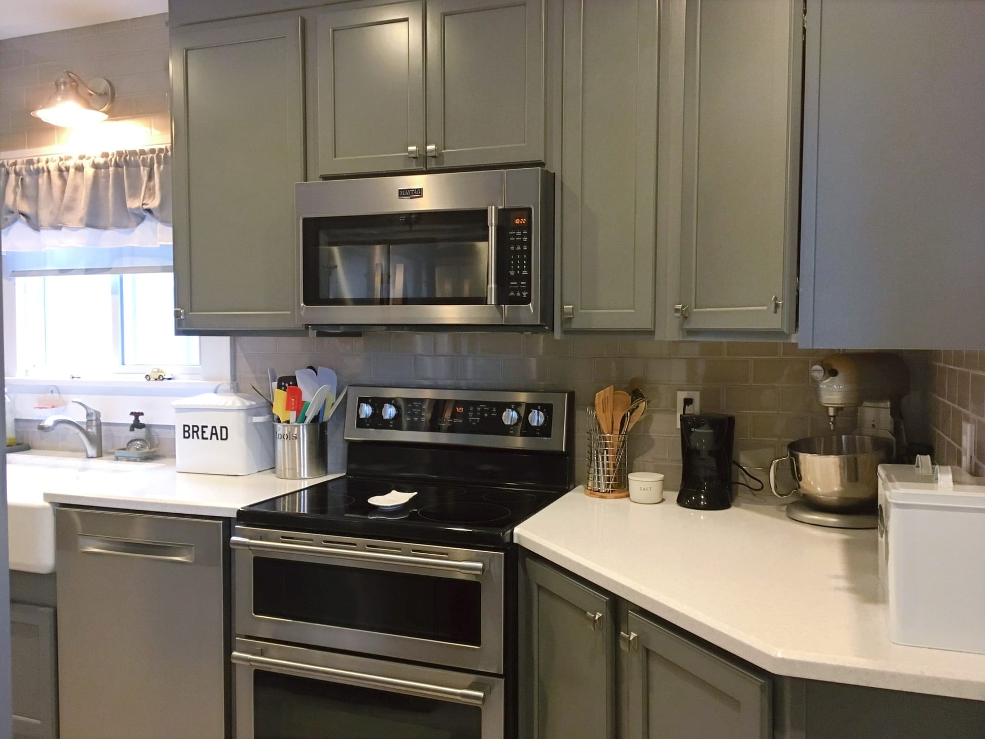 Grey shaker kitchen with stainless double-oven range, taupe subway tile backsplash, white quartz counters, and angled peninsula