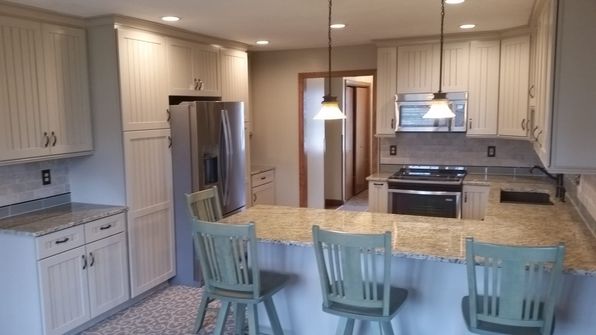 Cream kitchen with tan granite counters, peninsula breakfast bar, painted spindle-back stools, and stainless refrigerator, Erie County
