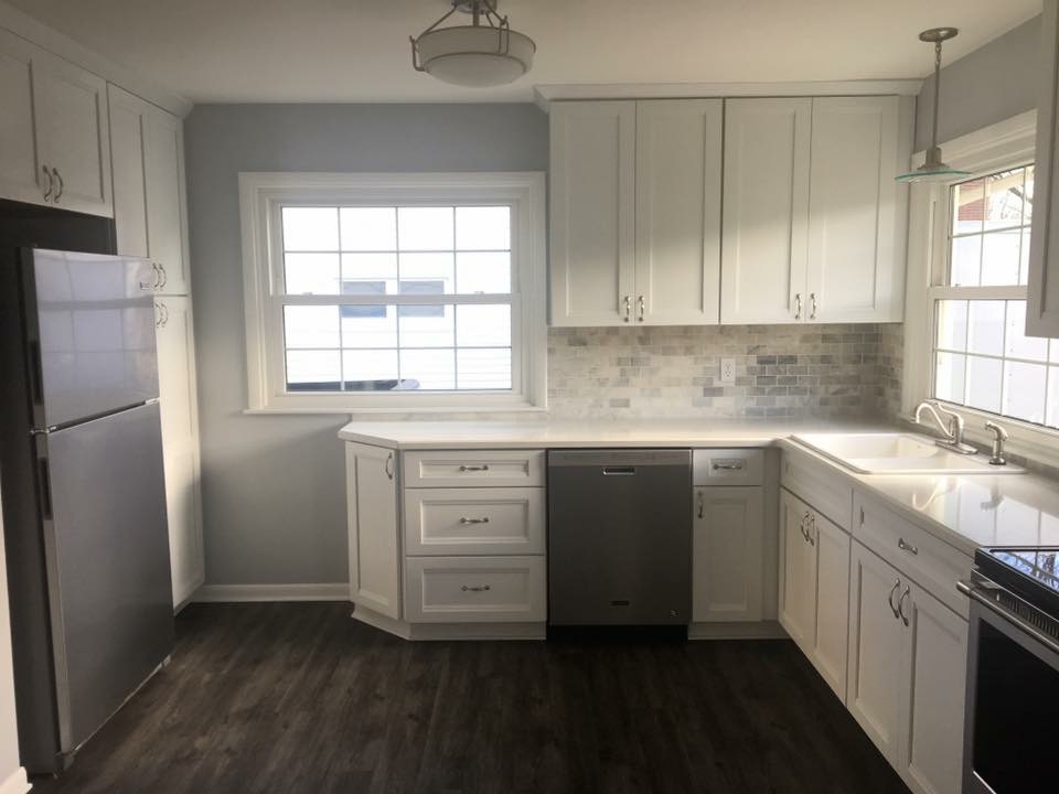 White shaker kitchen with grey marble-look tile backsplash, white counters, and dark wood-look plank flooring