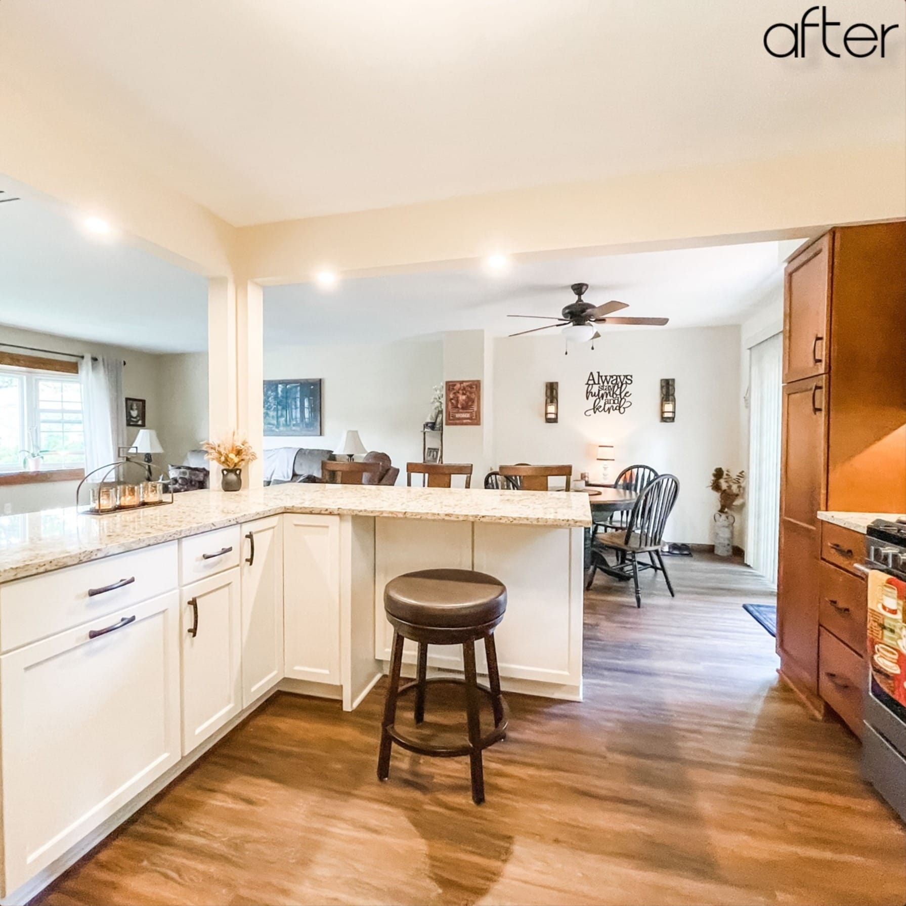 White shaker kitchen peninsula with tan granite counters, backless swivel stool, and wood-look plank flooring, open layout