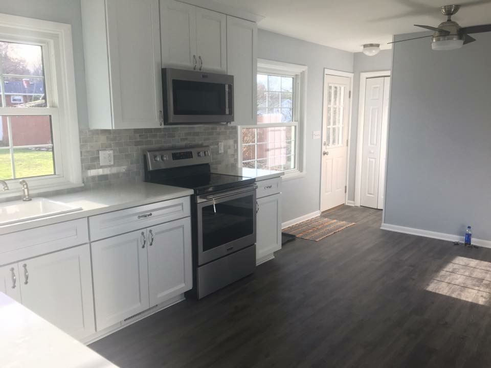 White shaker kitchen with grey marble-look subway tile, white quartz counters, stainless appliances, and dark plank flooring
