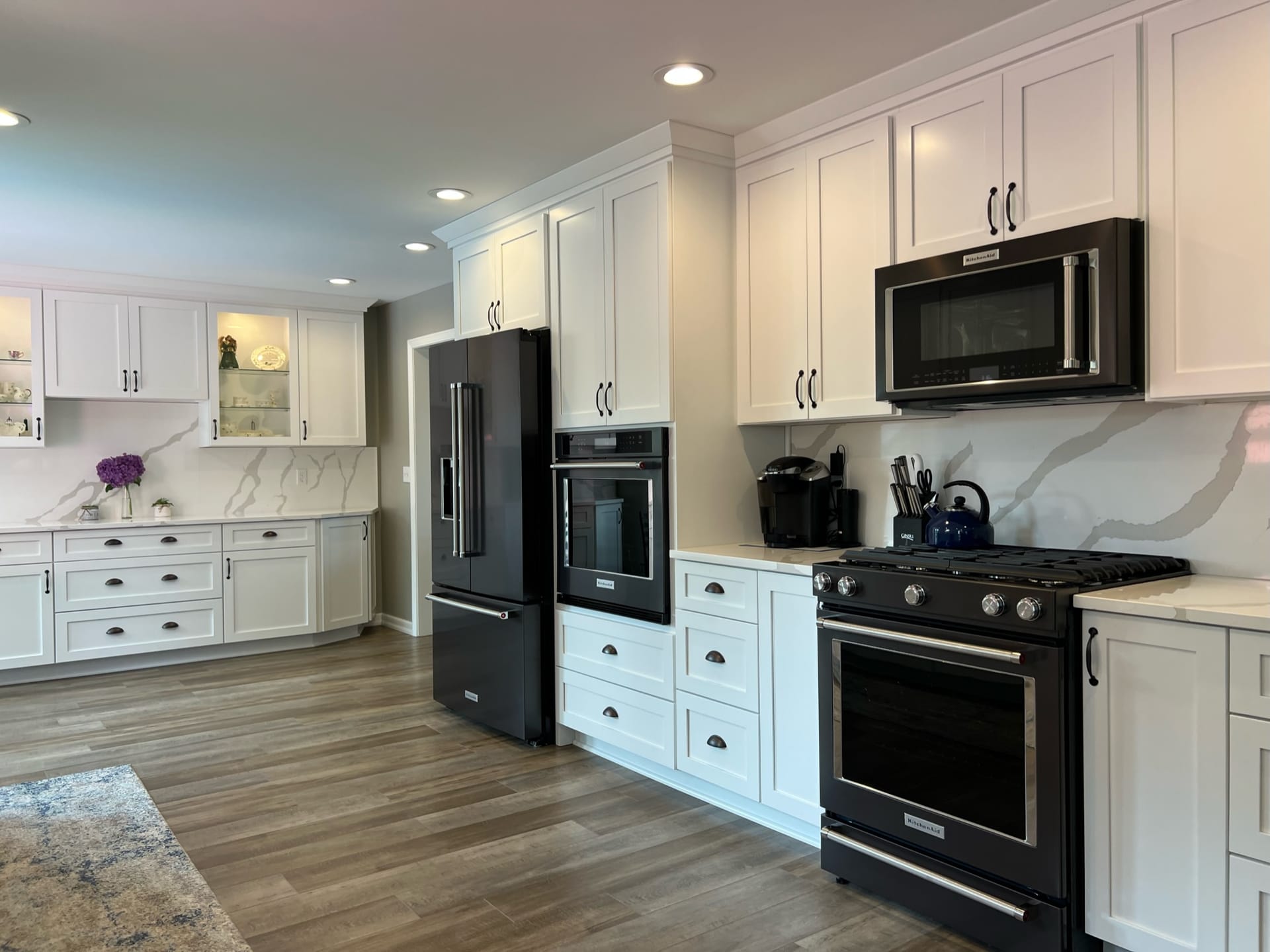 White shaker kitchen with white quartz counters, marble-look slab backsplash, black stainless appliances, wood-look plank flooring, Erie PA