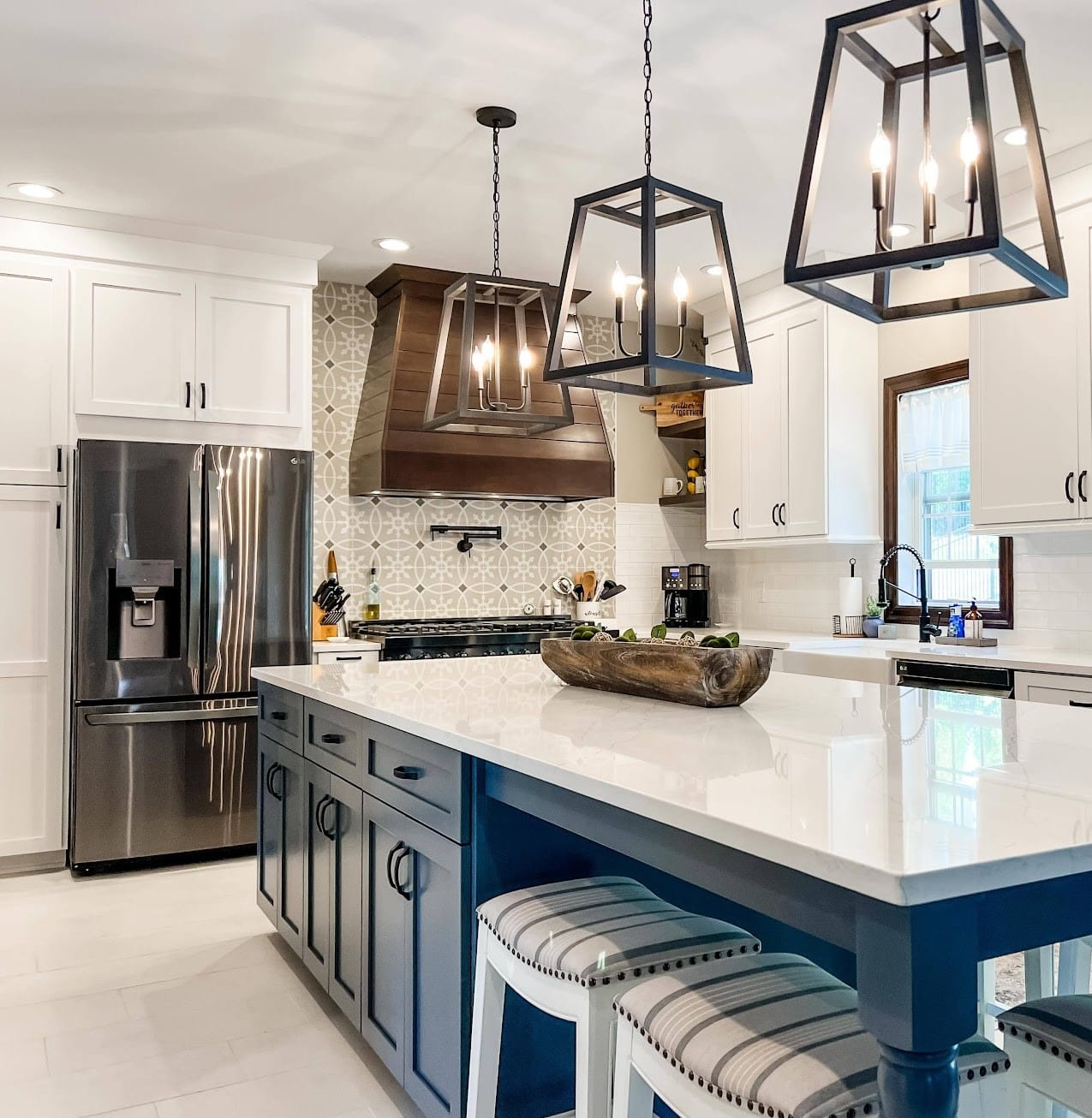 Two-tone kitchen with navy island, wood range hood, patterned tile backsplash, white quartz counters, and lantern pendants