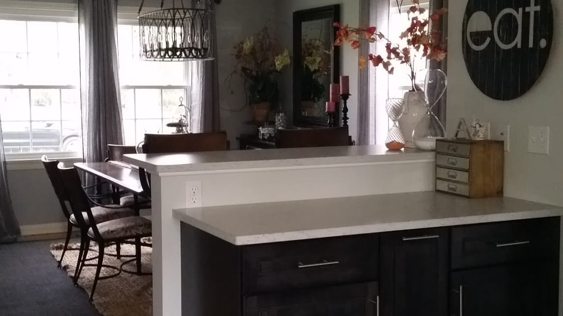 Dining nook with raised breakfast bar, dark wood cabinets, light stone counter, and adjacent farmhouse dining table