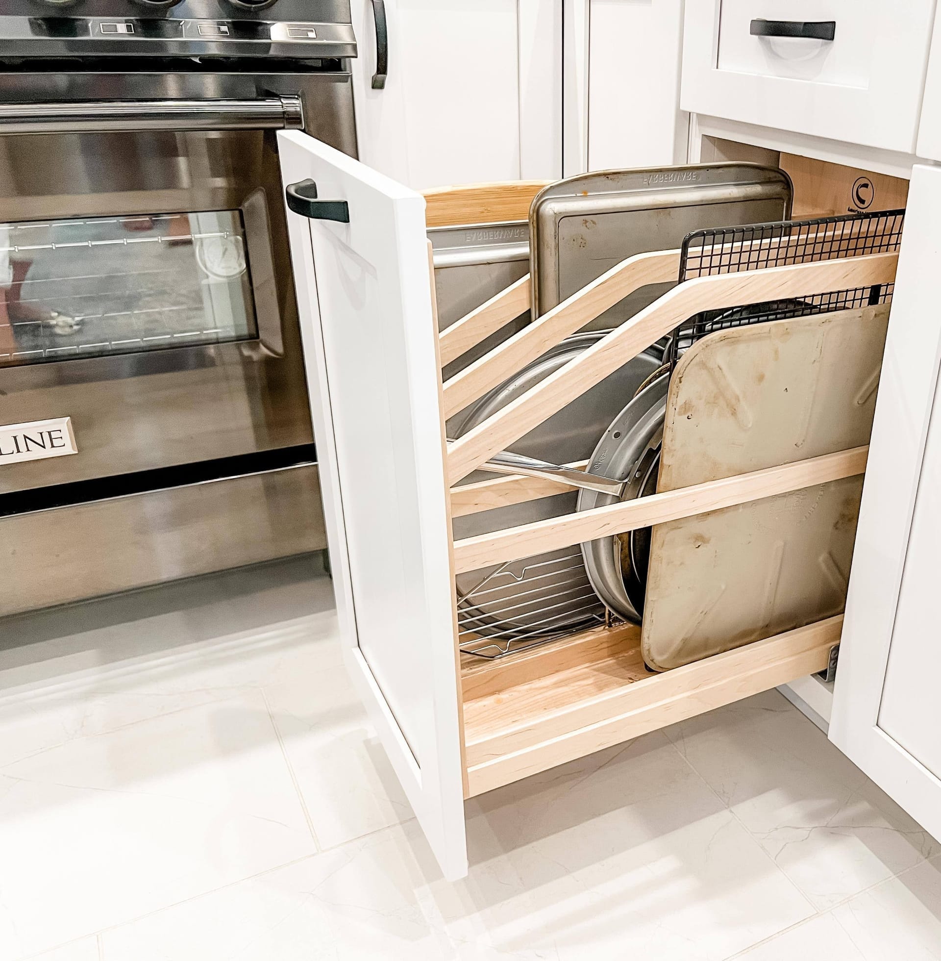Pull-out tray divider cabinet with vertical wood dividers for bakeware storage, in a white shaker kitchen