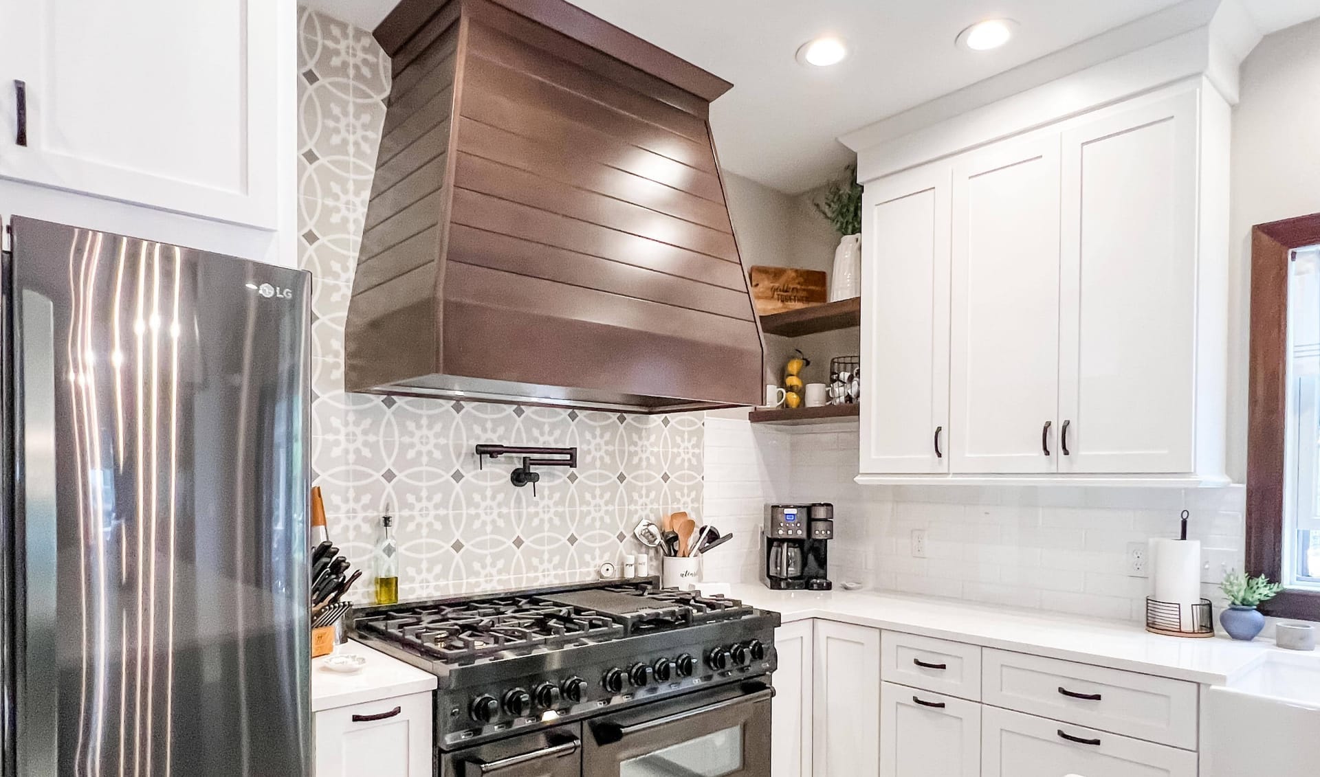 White shaker kitchen with copper range hood, patterned cement-tile backsplash, white quartz counters, and professional gas range