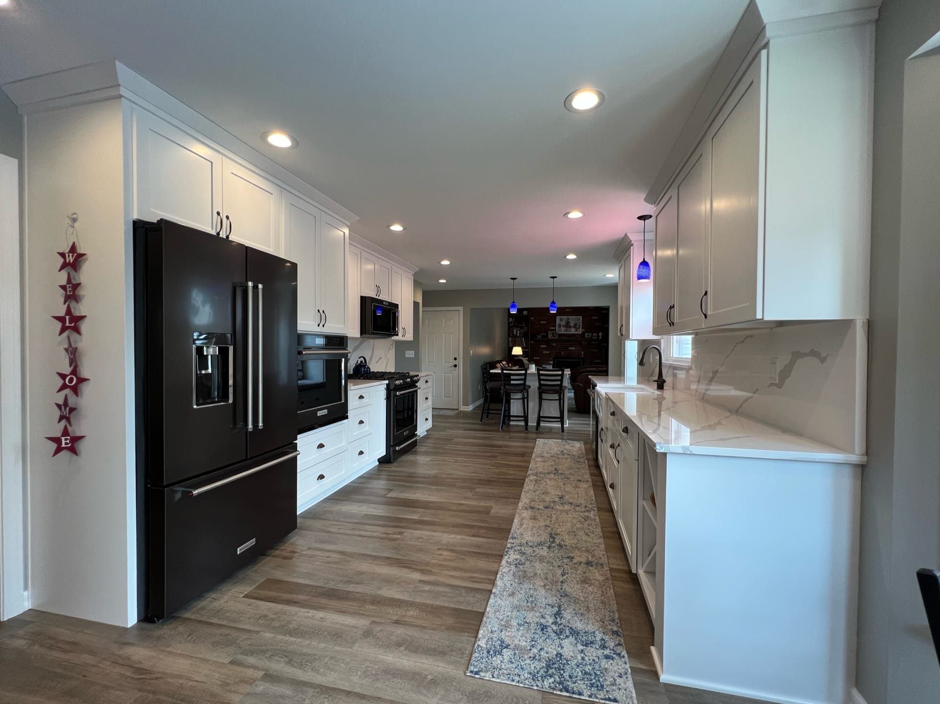 White shaker kitchen with black appliances, marble-look quartz counters, wood-look plank flooring, and open dining area