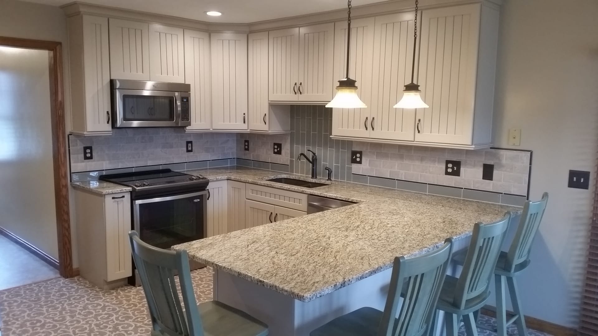 Cream kitchen with tan granite peninsula, grey subway tile backsplash, spindle-back stools, and stainless appliances, Erie County