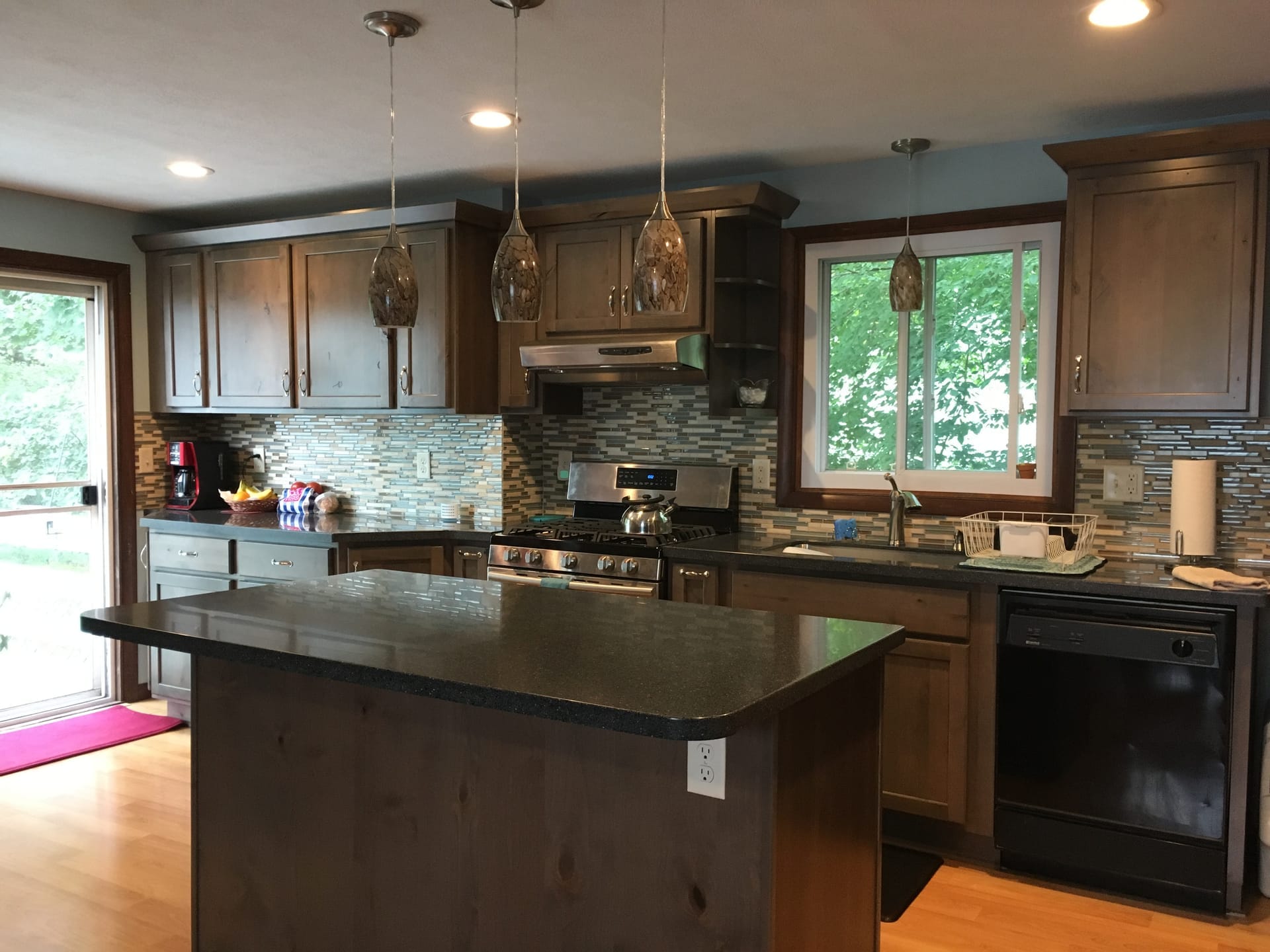 Grey-stained wood kitchen with linear glass mosaic backsplash, dark granite counters, wood island, and hardwood flooring, Erie PA