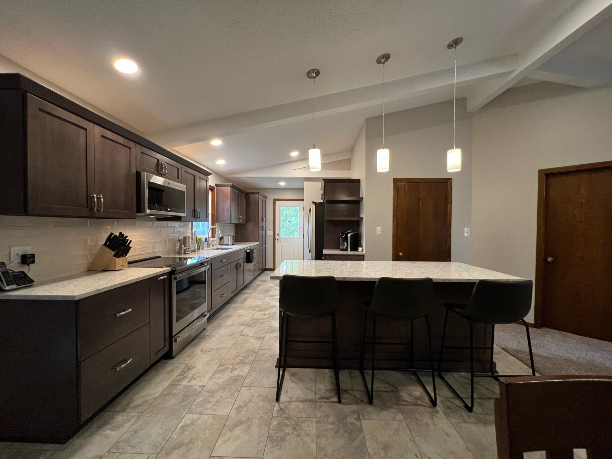 Dark-stained shaker kitchen with grey stone counters, subway tile backsplash, stainless appliances, and seated island, Erie County
