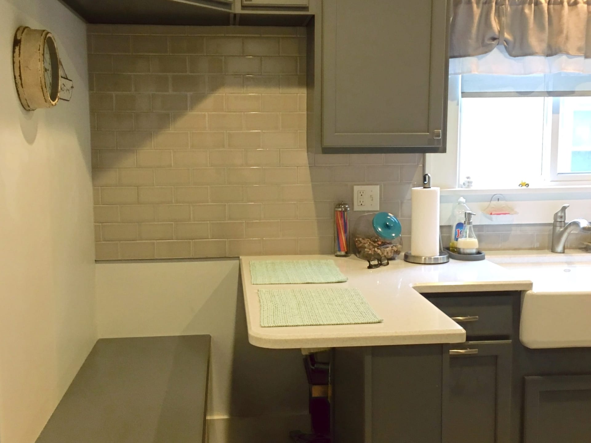 Grey shaker kitchen with greige subway tile, white quartz peninsula, farmhouse apron sink, and window seat, Edinboro