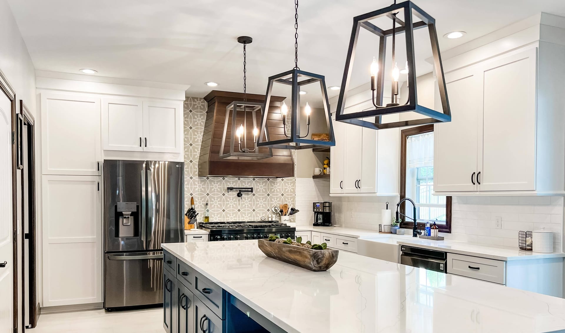 White shaker kitchen with navy island, wood range hood, mosaic backsplash, white quartz counters, and lantern pendants