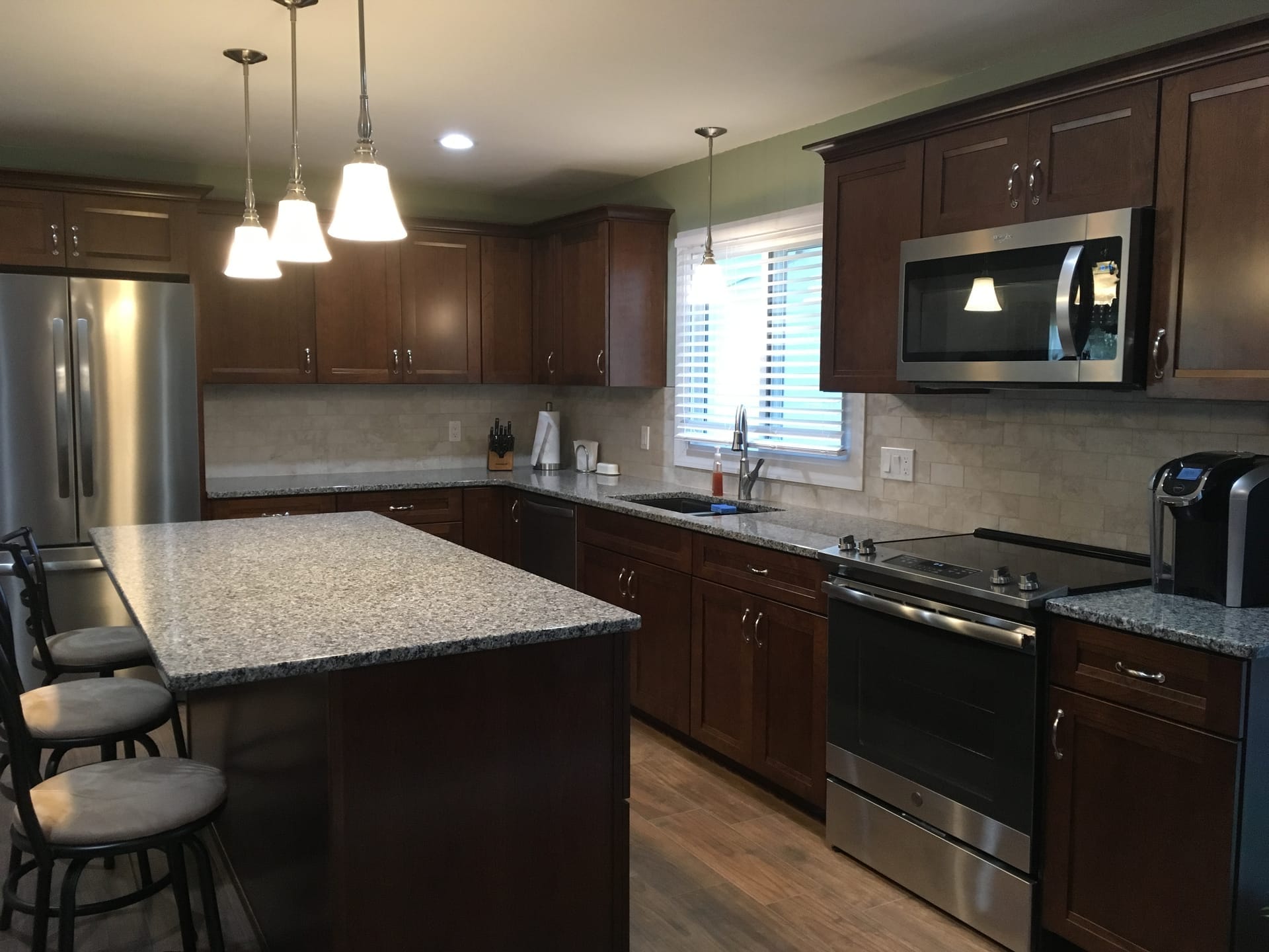 Espresso shaker kitchen with greige subway tile, speckled granite island, stainless appliances, and wood-look plank flooring, Erie PA