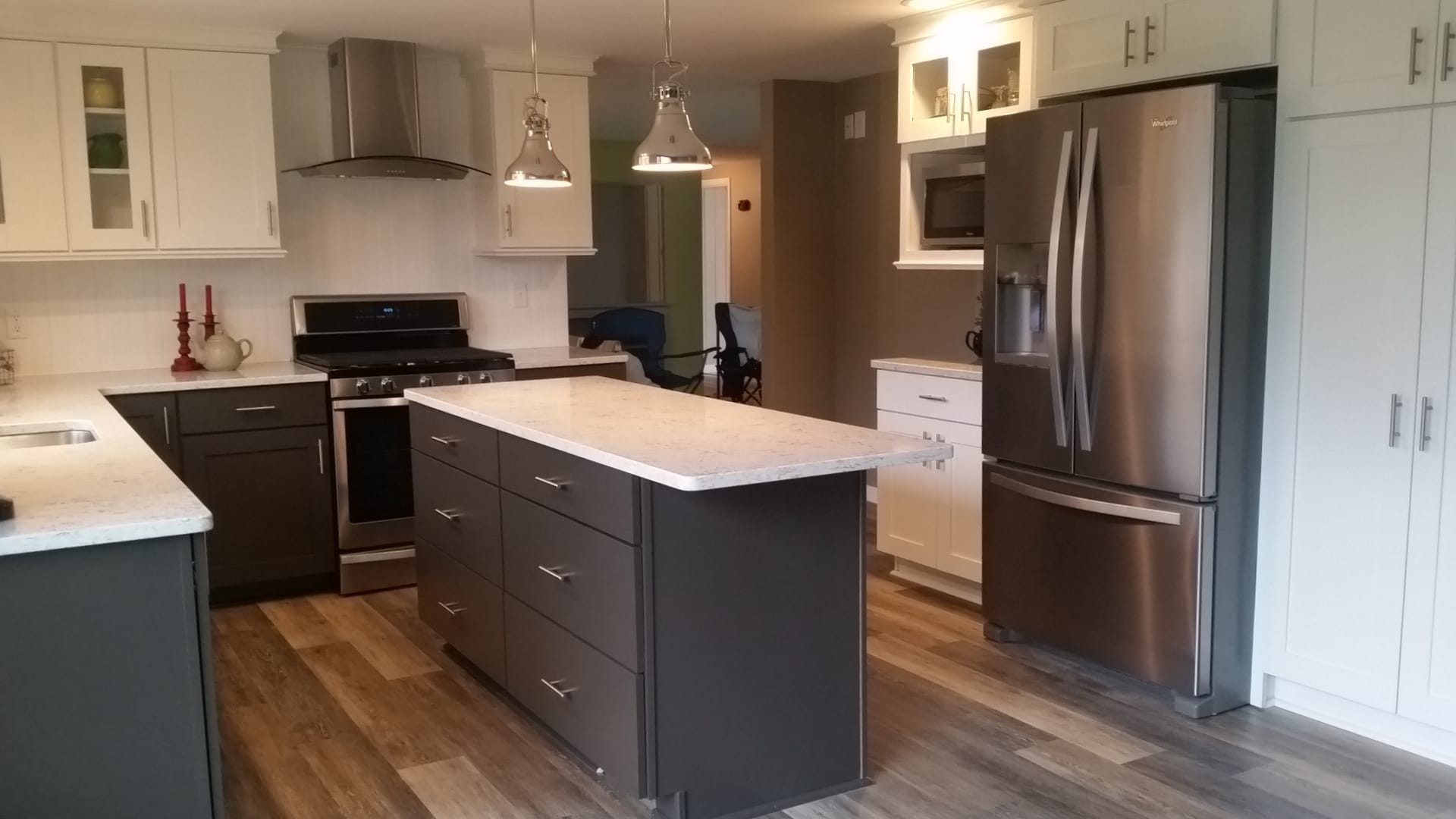 Two-tone kitchen with white perimeter cabinets, grey island, stainless chimney hood, white subway tile, and plank flooring