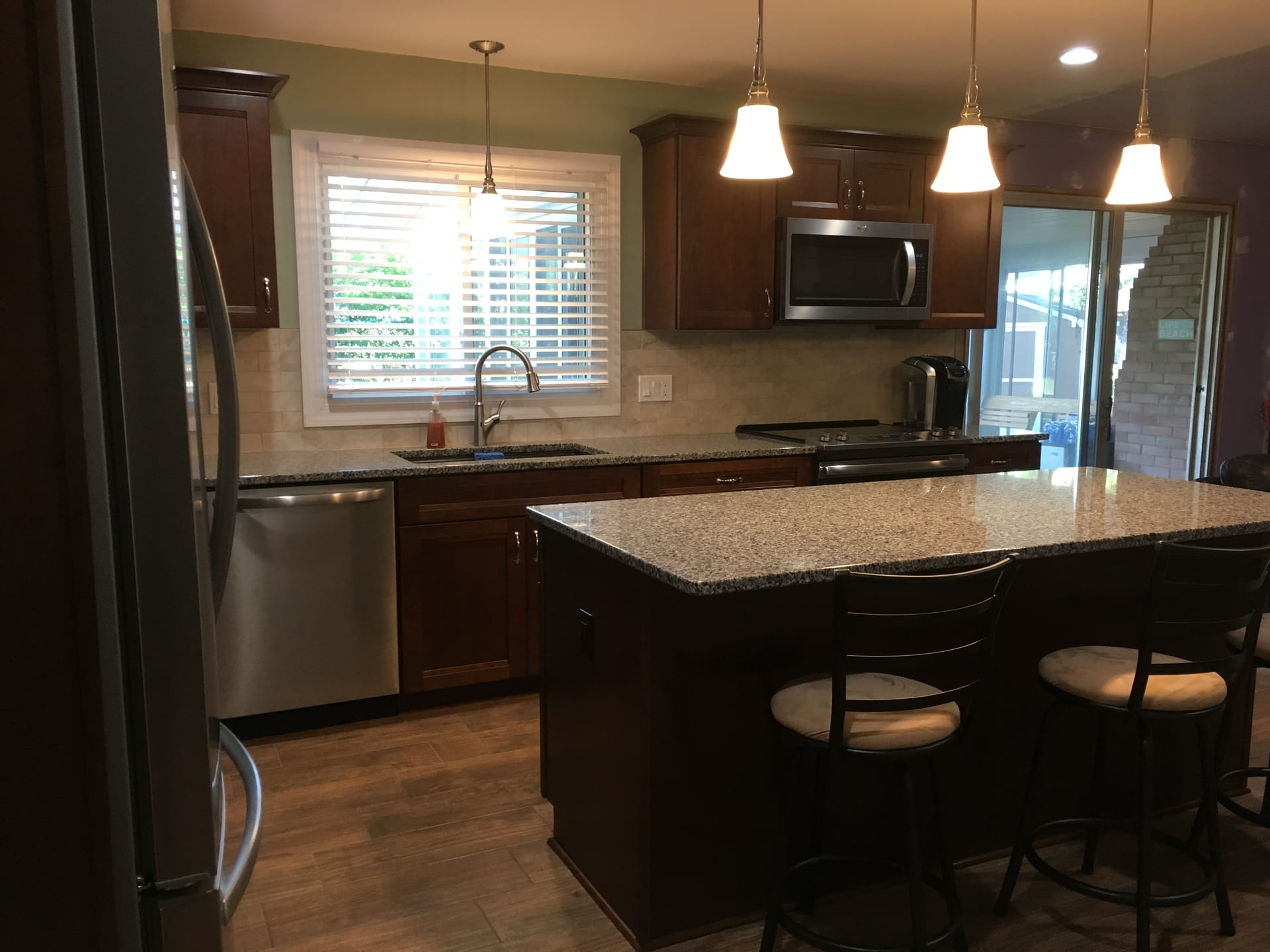 Cherry-toned shaker kitchen with travertine subway tile, speckled granite island, stainless dishwasher, and wood-look plank flooring, Erie County