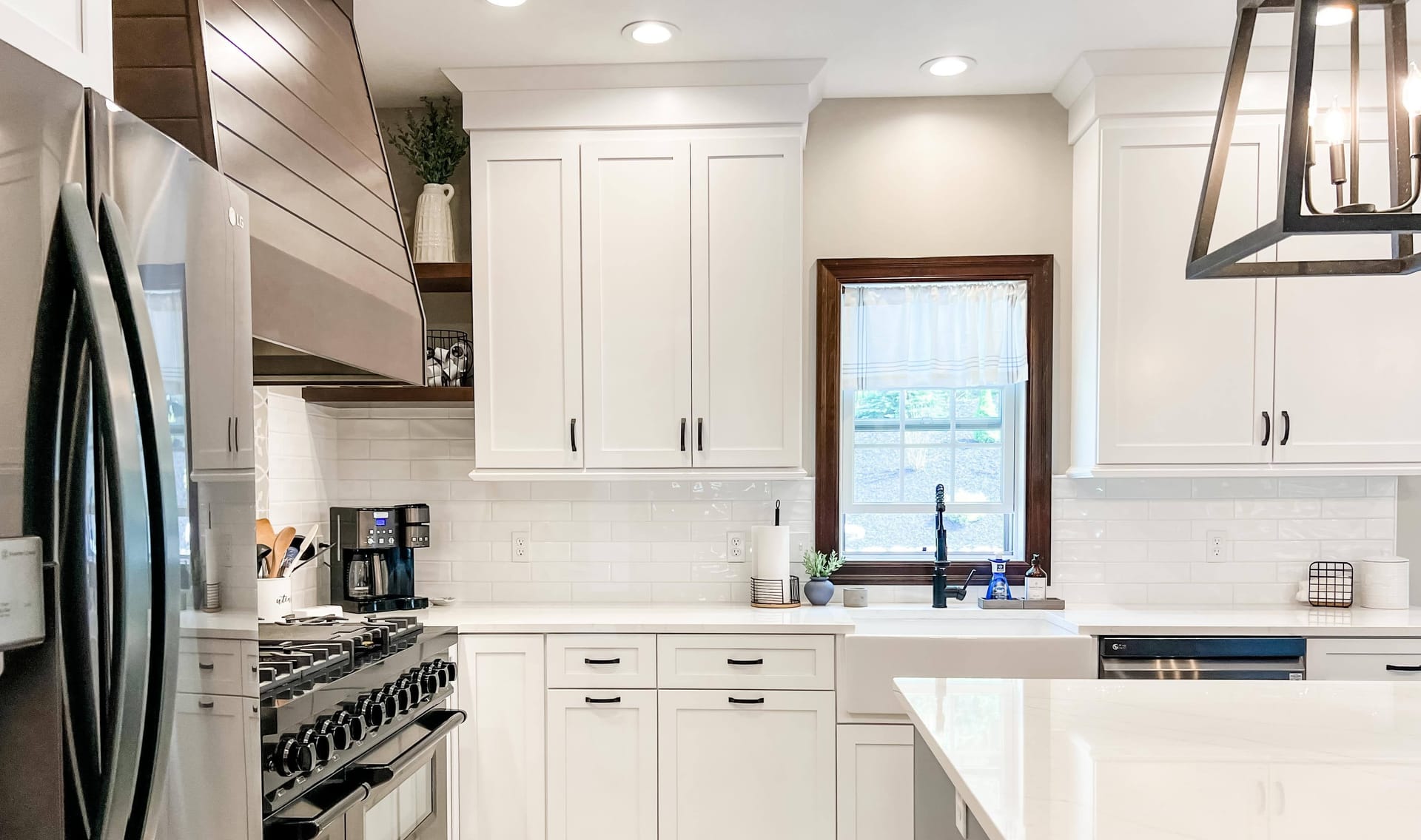 White shaker kitchen with wood range hood, white subway tile, white quartz island, and professional gas range