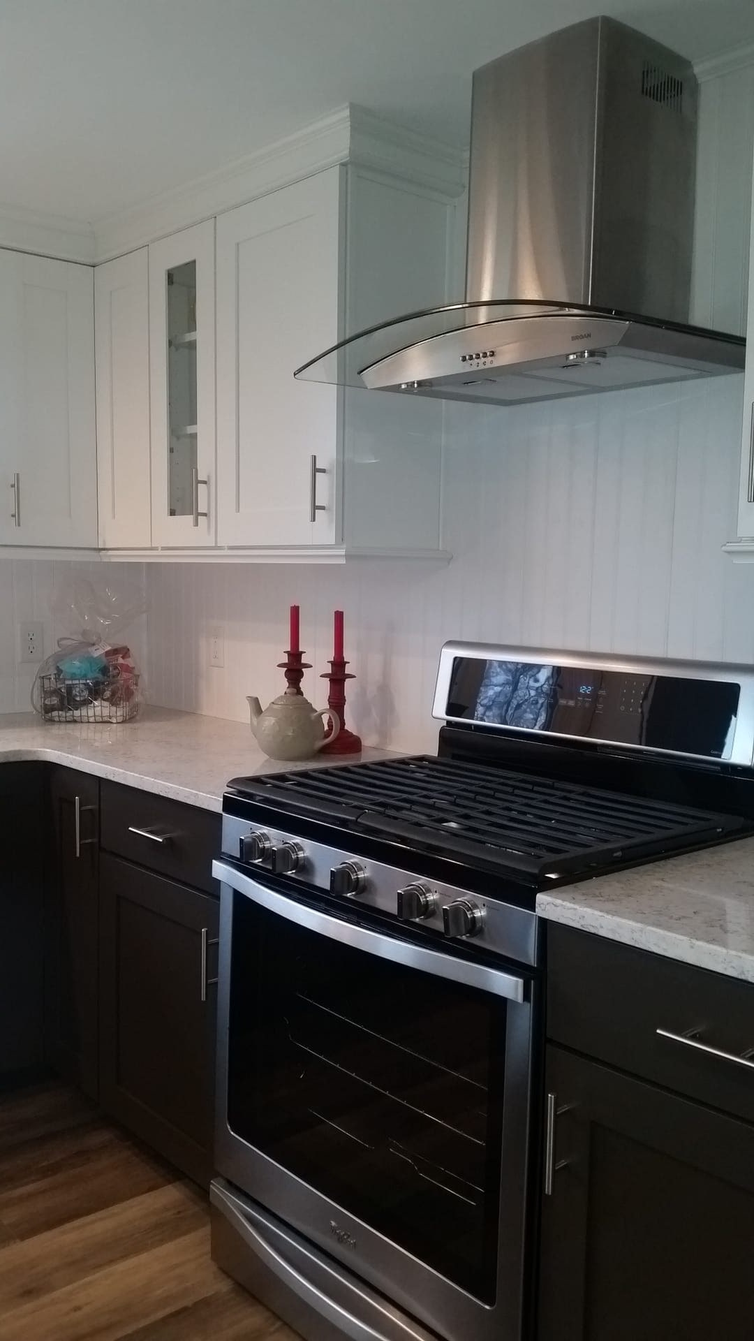 Kitchen with stainless chimney range hood, white plank backsplash, dark cabinetry, and stainless gas range