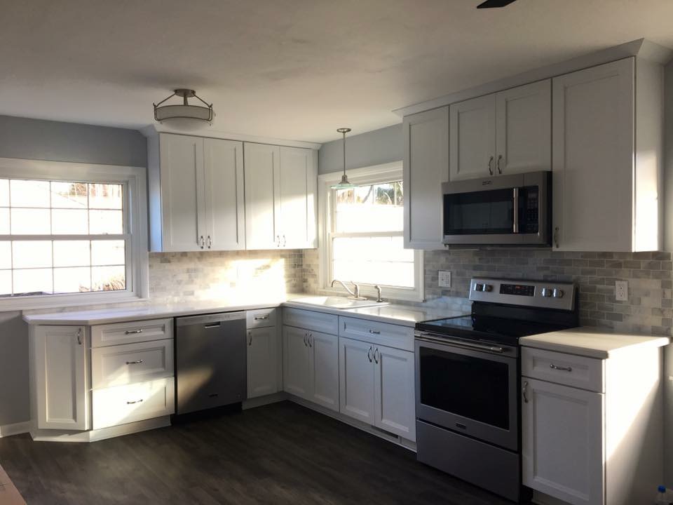 White shaker kitchen with grey marble-look subway tile, white quartz counters, stainless appliances, dark plank flooring, Erie County