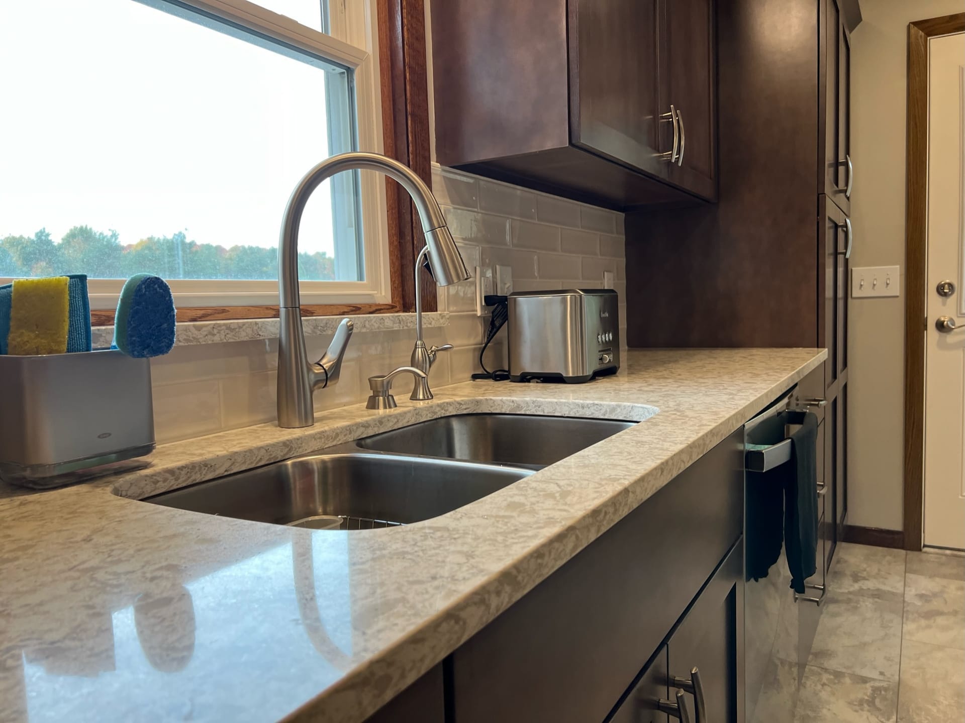Stainless undermount sink with gooseneck faucet, greige counters, grey subway tile, and espresso cabinetry