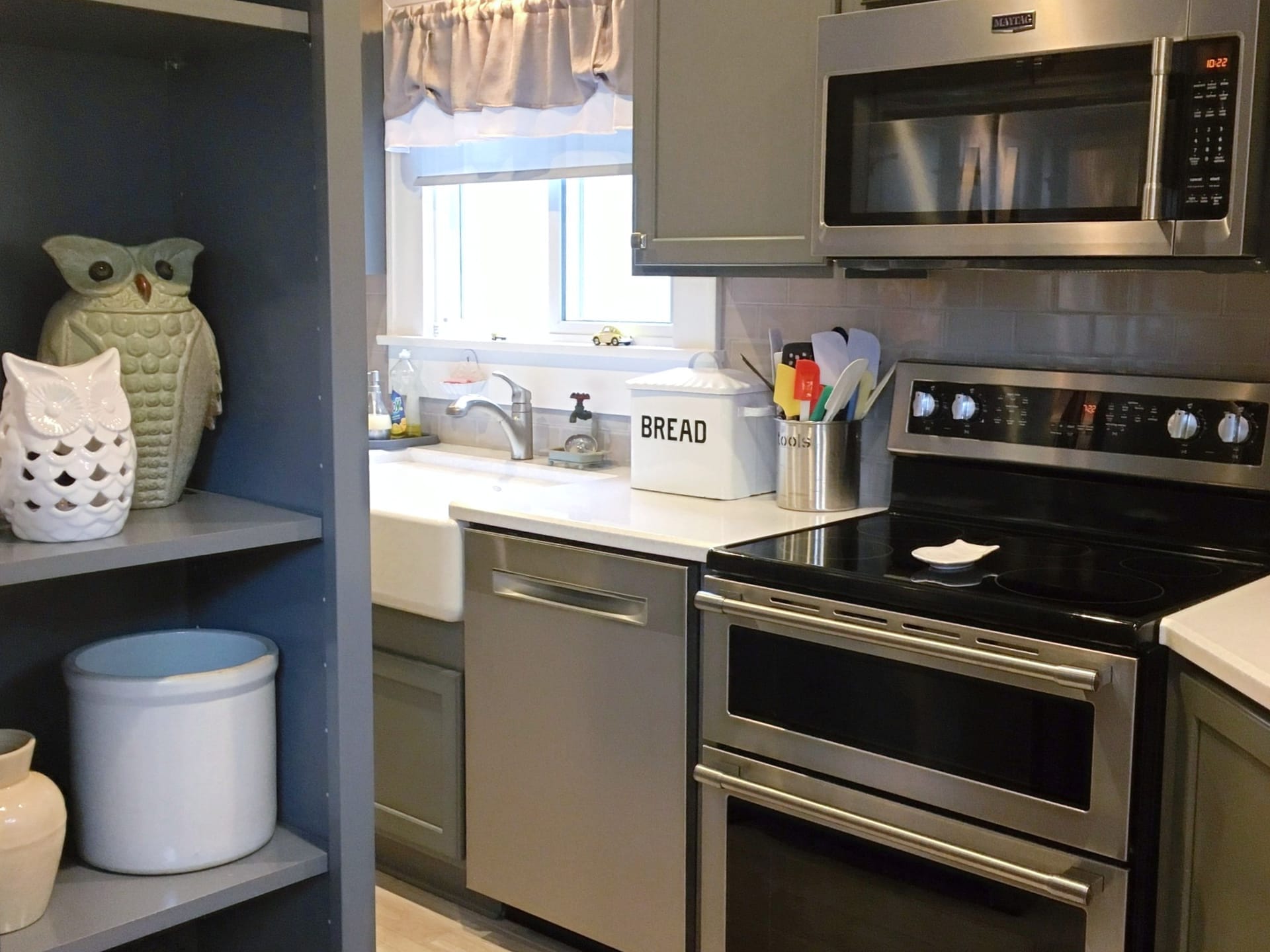 Grey shaker kitchen with open shelving, farmhouse apron sink, stainless double-oven range, and taupe subway tile, Erie PA