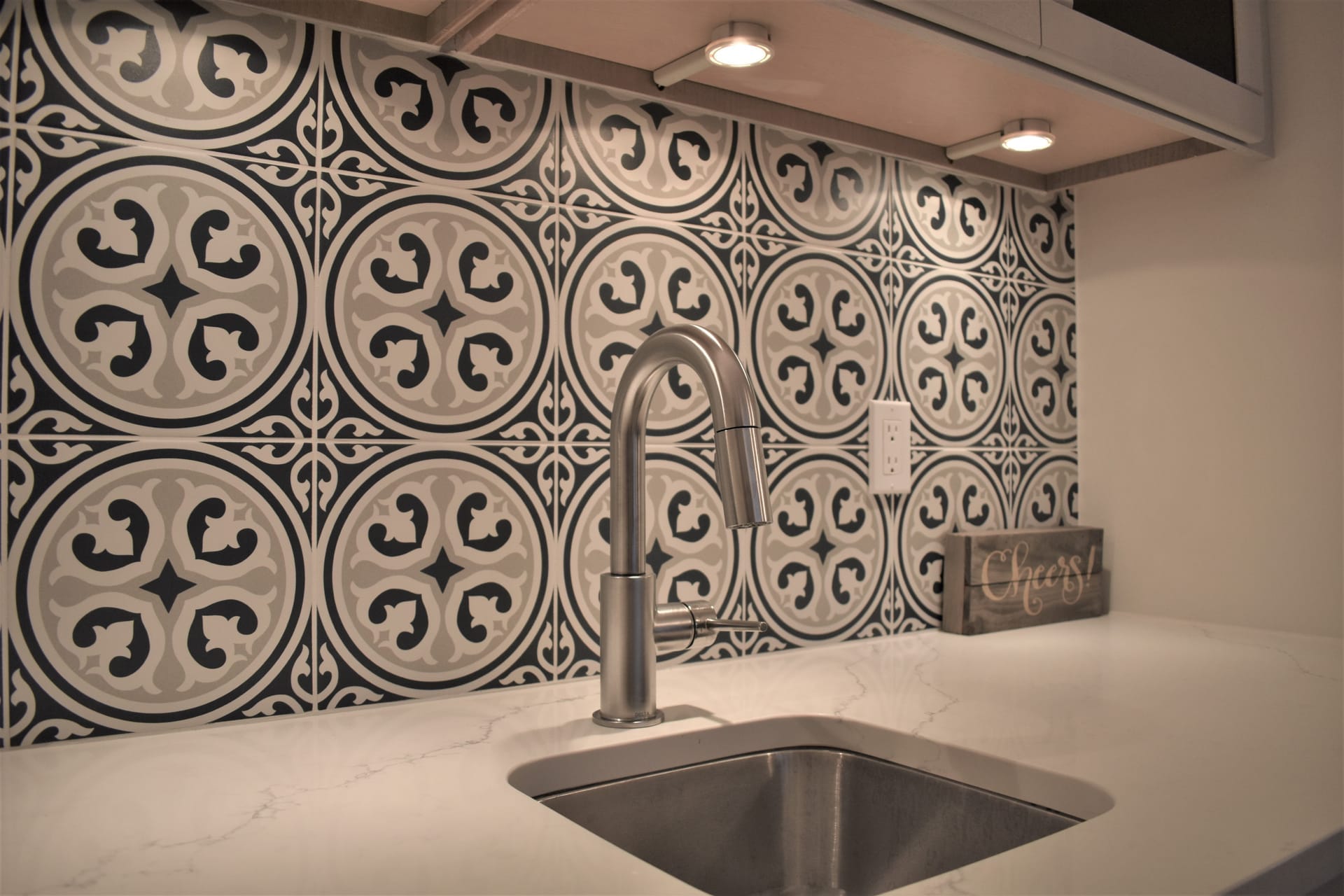 Black-and-white patterned cement tile backsplash with stainless bar sink, gooseneck faucet, and white quartz counter