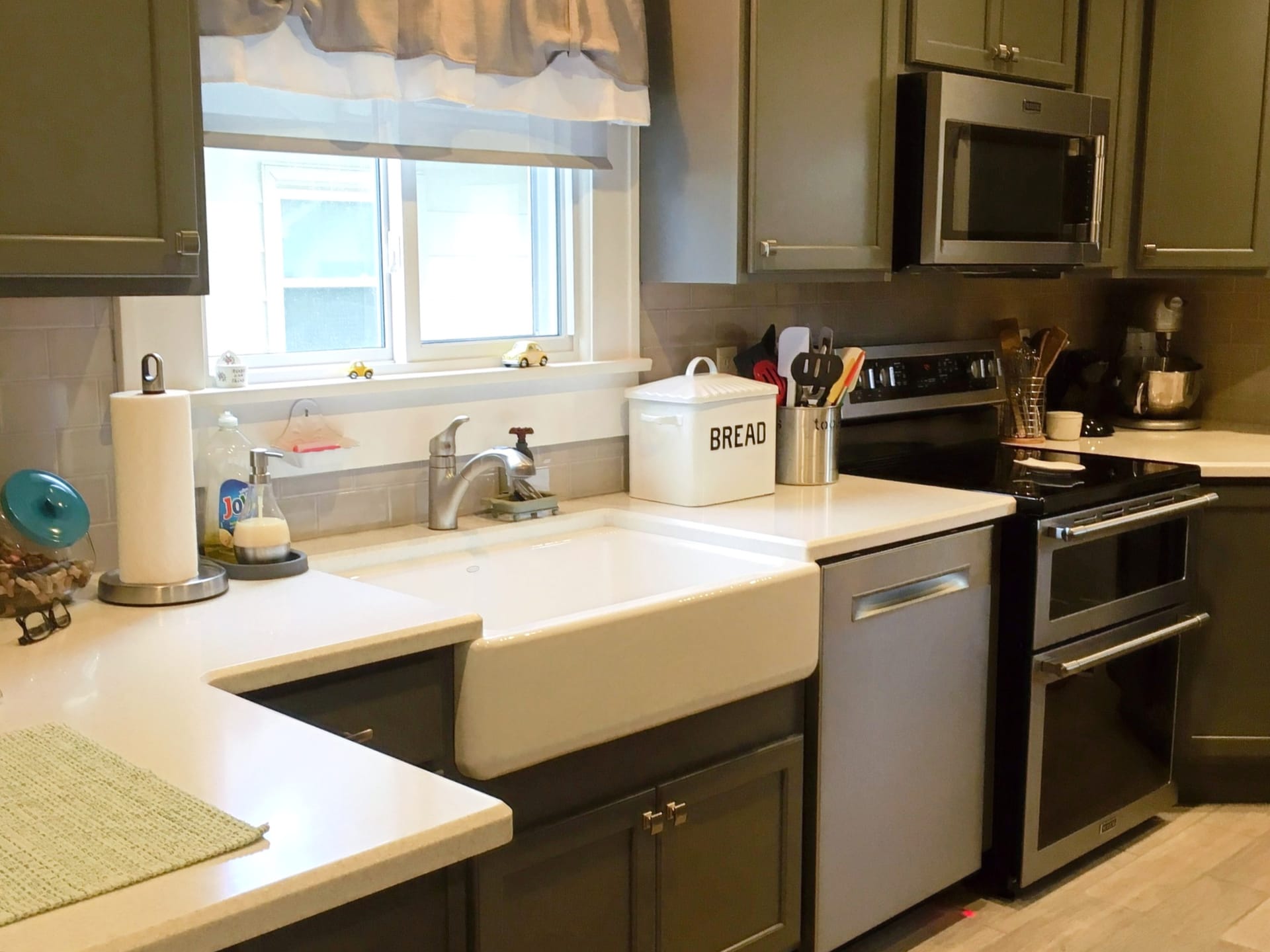 Sage green shaker kitchen with taupe subway tile, white quartz counters, farmhouse apron sink, and stainless double-oven range