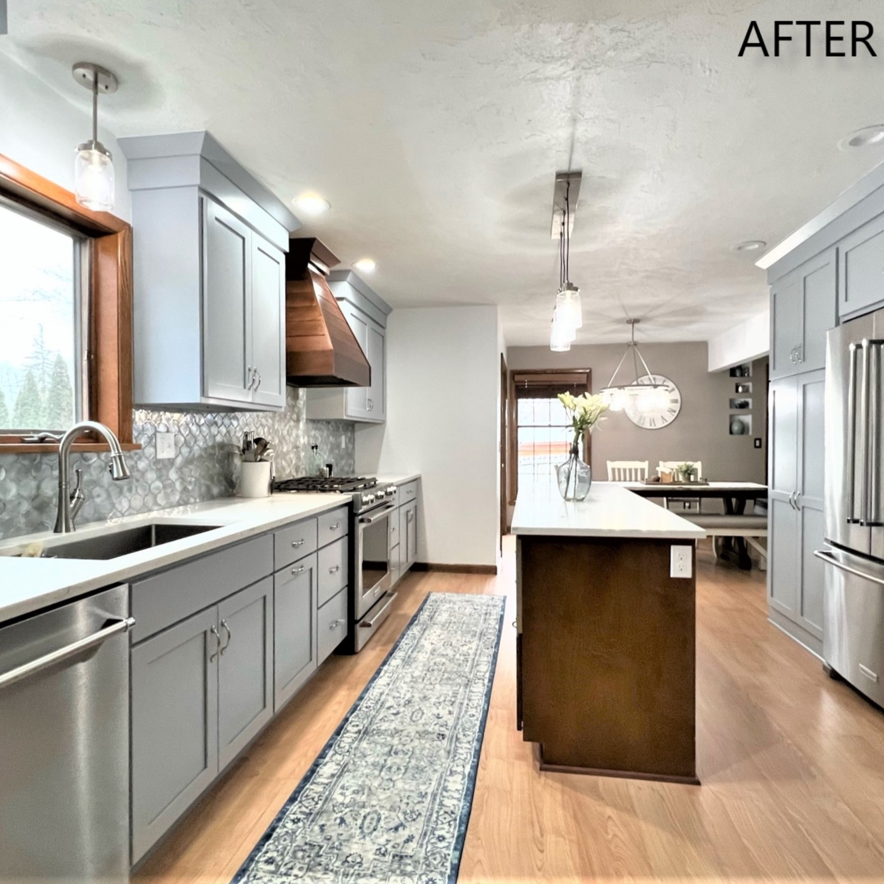 Galley kitchen with light blue-grey cabinets, white quartz counters, wood range hood, dark stained island, and hardwood flooring