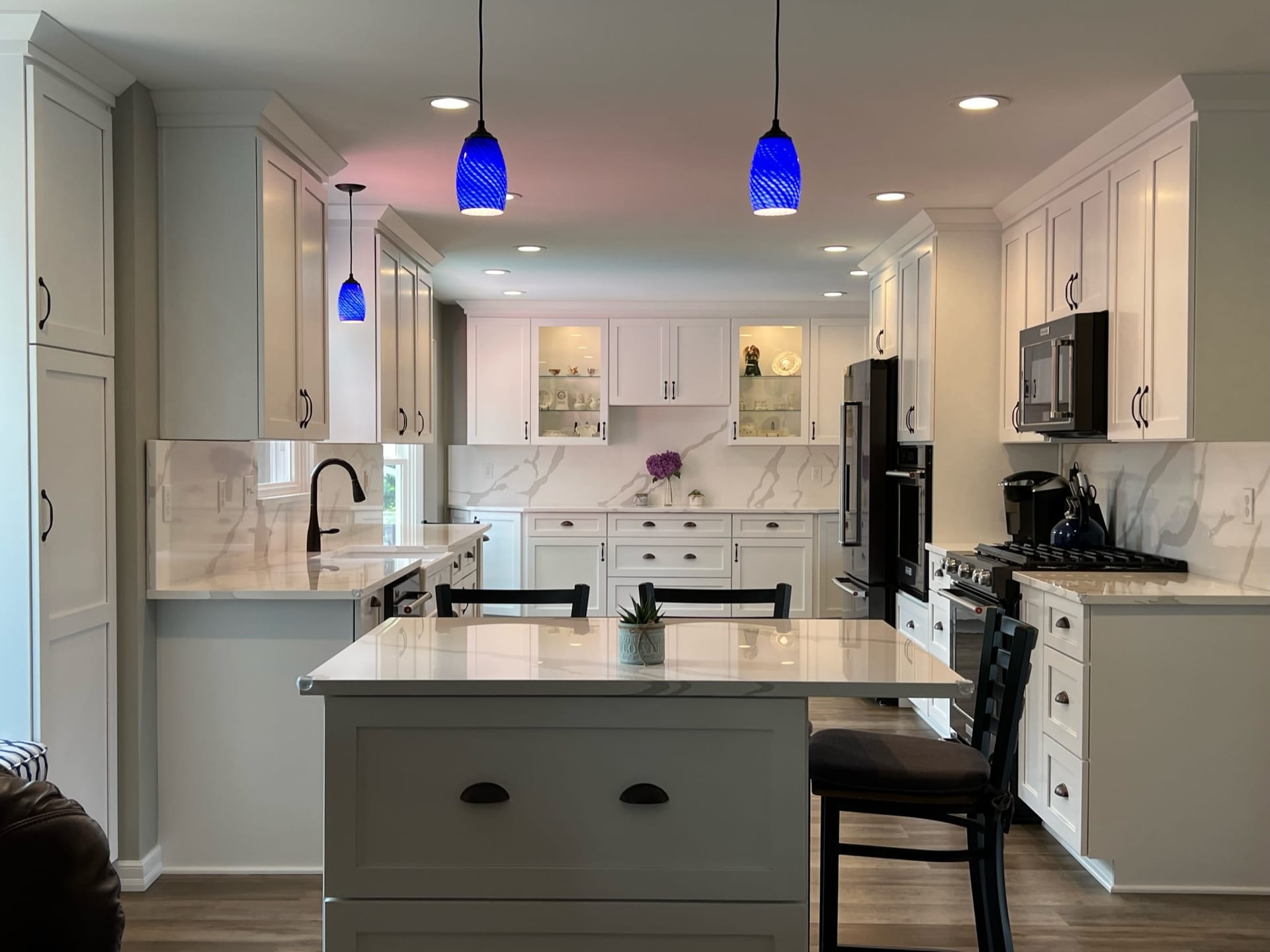White shaker kitchen with marble-look quartz counters, slab backsplash, grey island, black appliances, and glass-front cabinets, Erie County