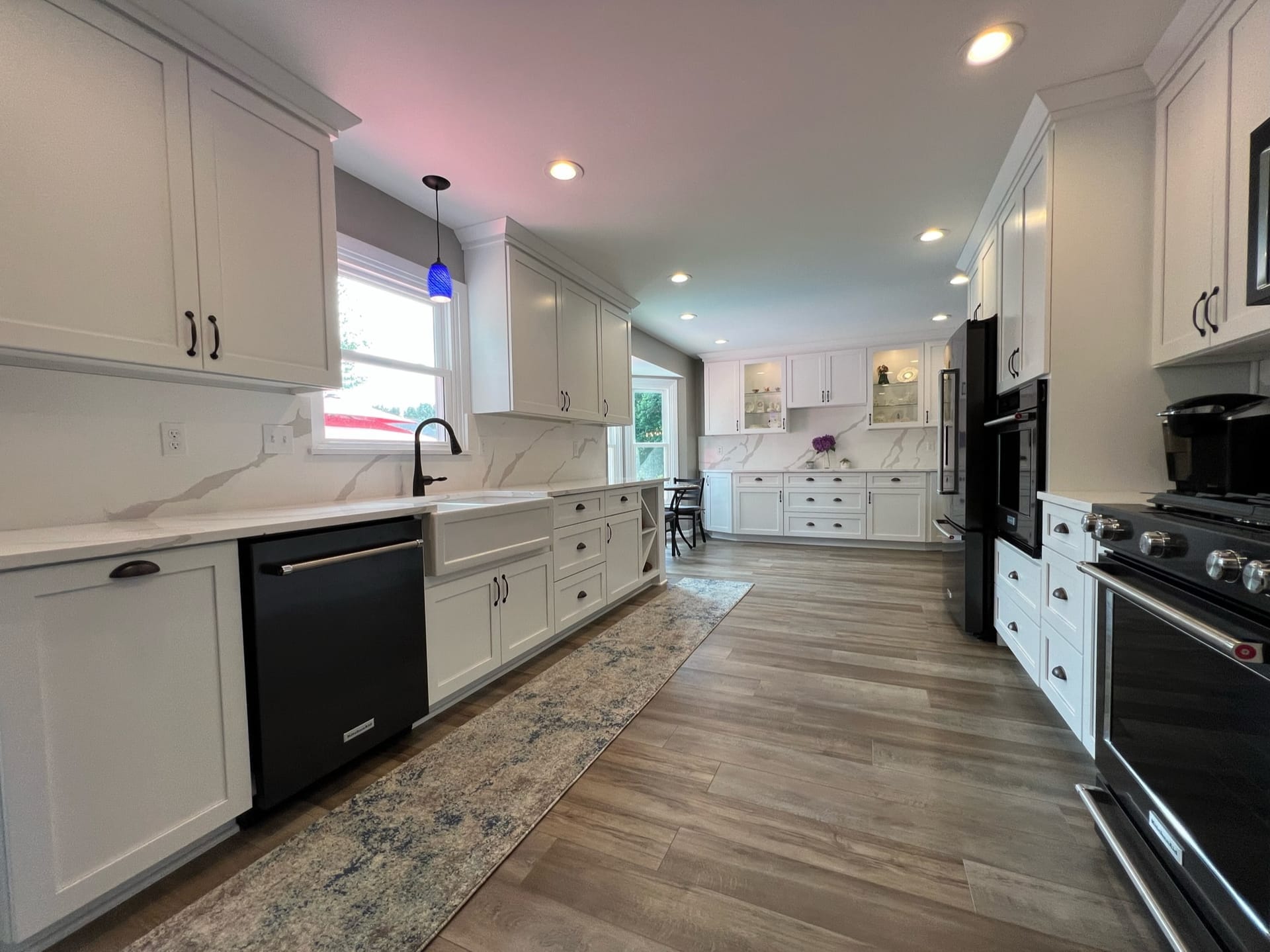 White shaker kitchen with marble-look quartz counters, farmhouse apron sink, black appliances, and wood-look plank flooring