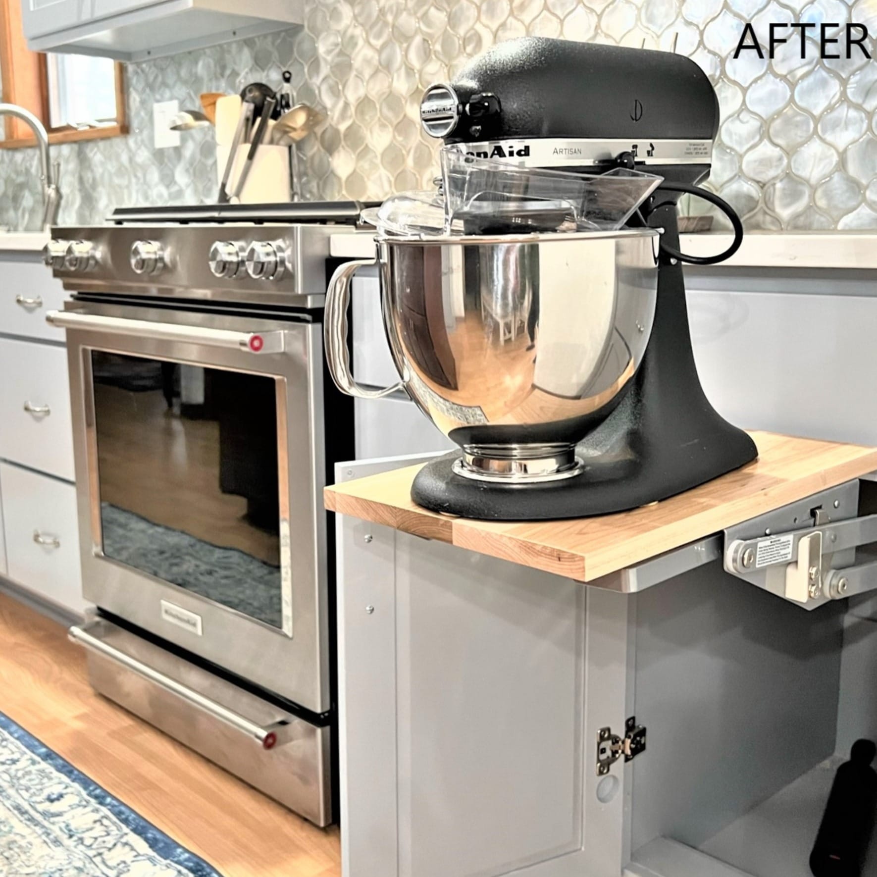 Grey shaker cabinet with pull-out mixer lift shelf beside a stainless gas range, silver mosaic backsplash