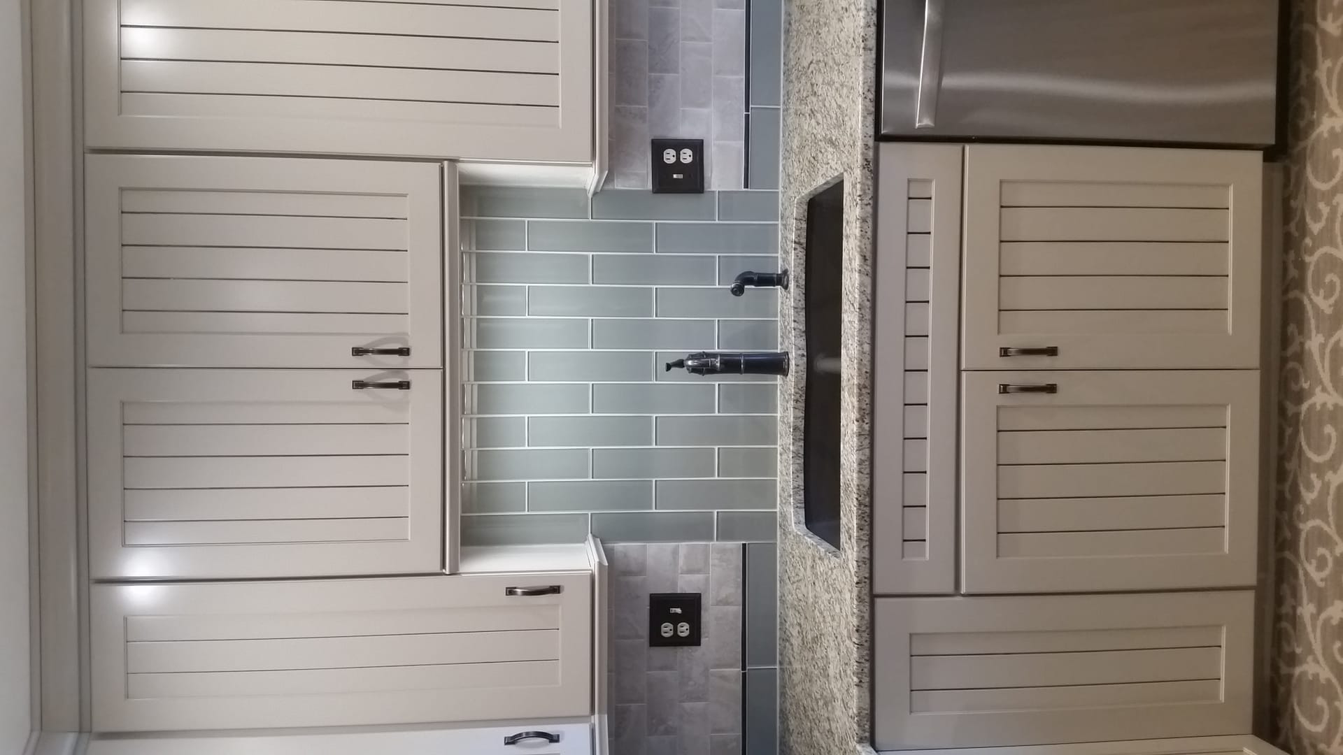 Cream plank-front cabinets with grey-blue subway tile backsplash, granite counter, and stainless refrigerator, Edinboro