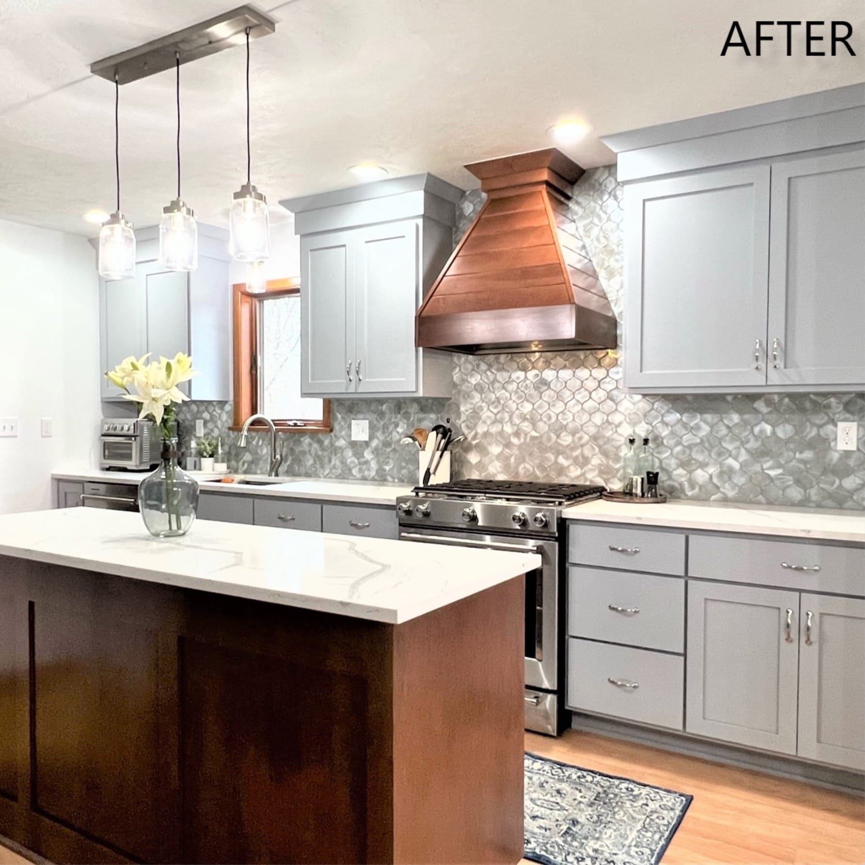 Grey shaker kitchen with copper range hood, silver mosaic backsplash, white quartz counters, wood island, and glass pendants