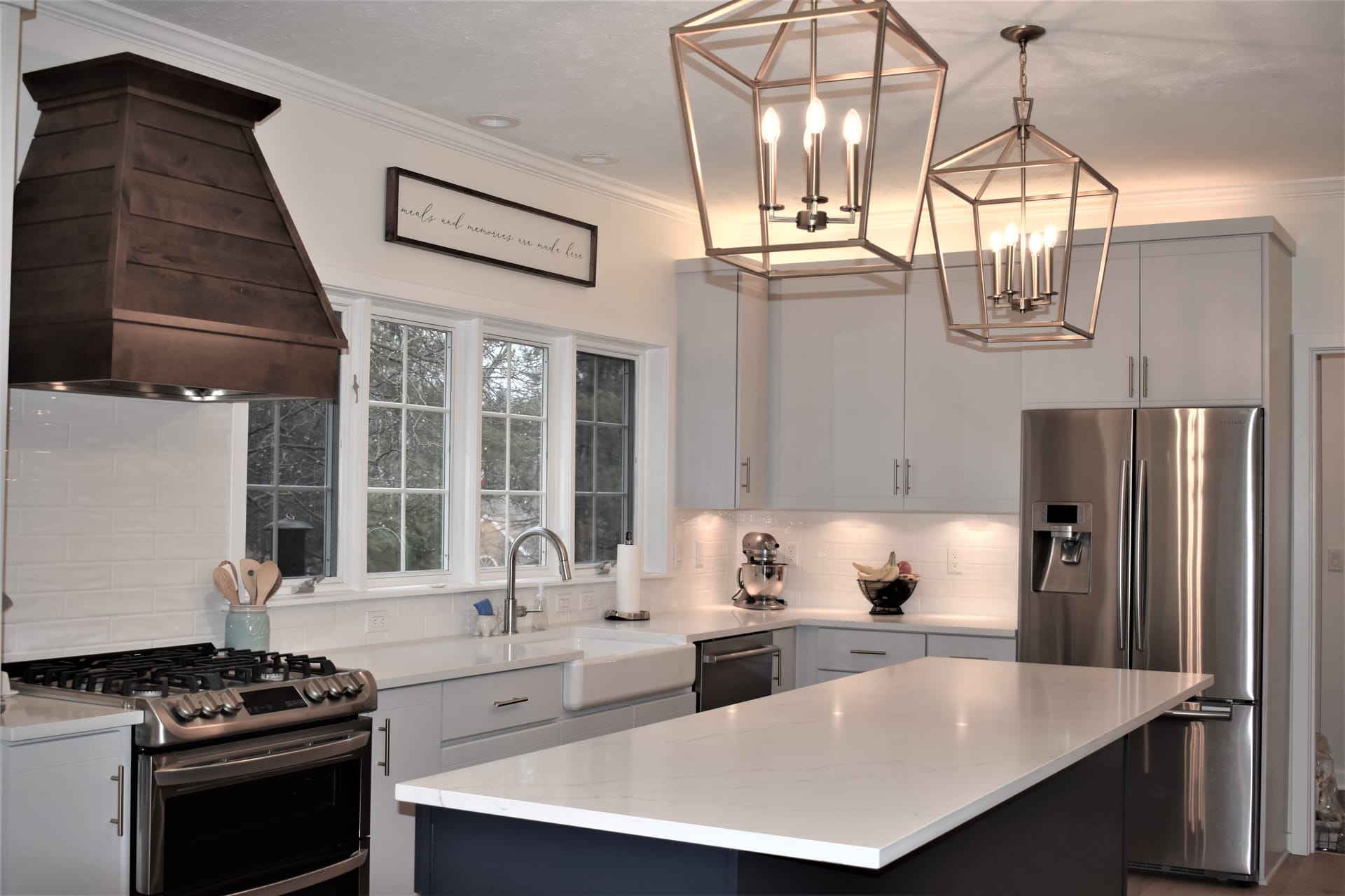 White shaker kitchen with dark wood range hood, white subway tile, navy island, and gold lantern pendants