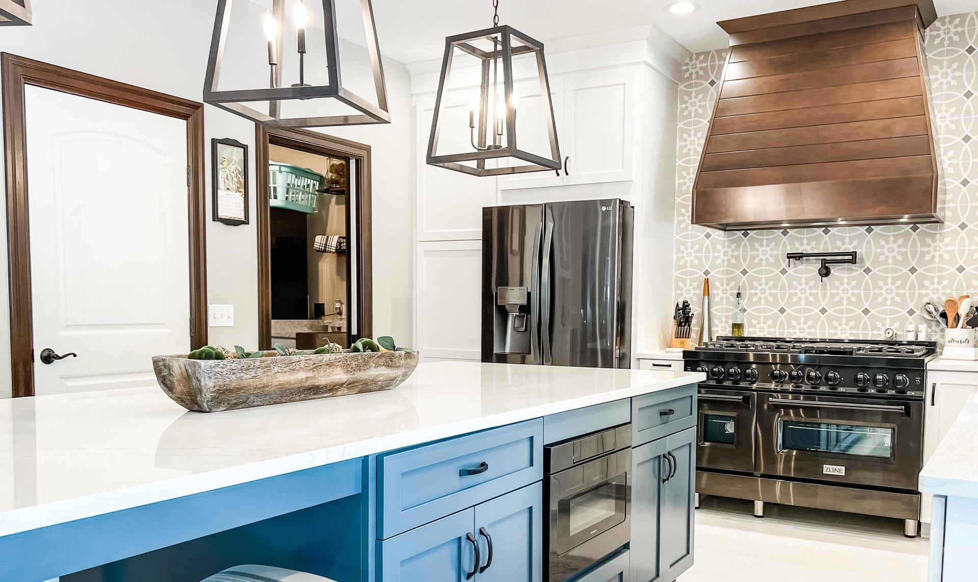 White shaker kitchen with blue island, wood range hood, patterned cement tile backsplash, white quartz counters, lantern pendants