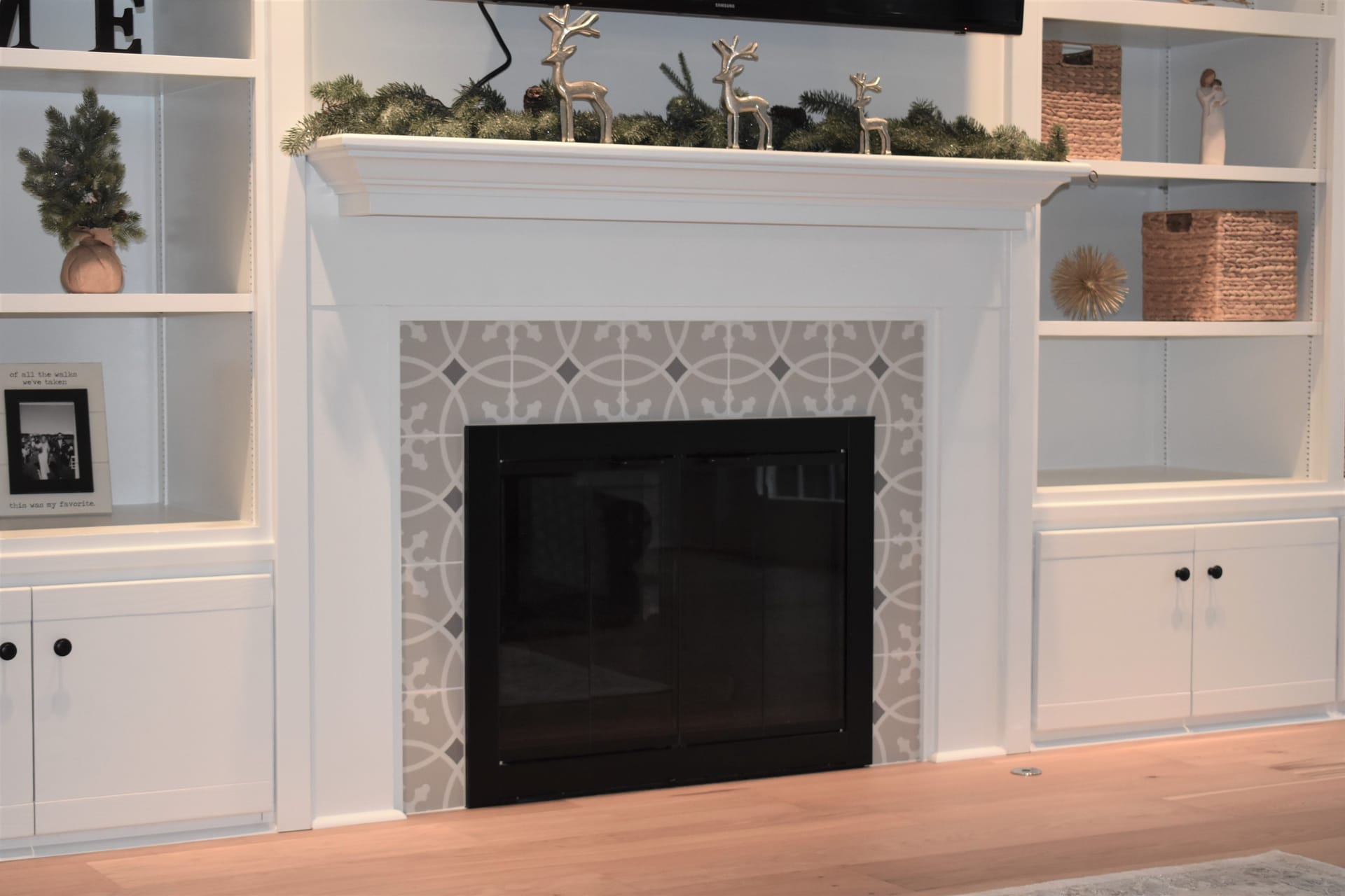 White built-in shelving flanking a fireplace with grey patterned tile surround, white mantel, and plank flooring, Erie PA